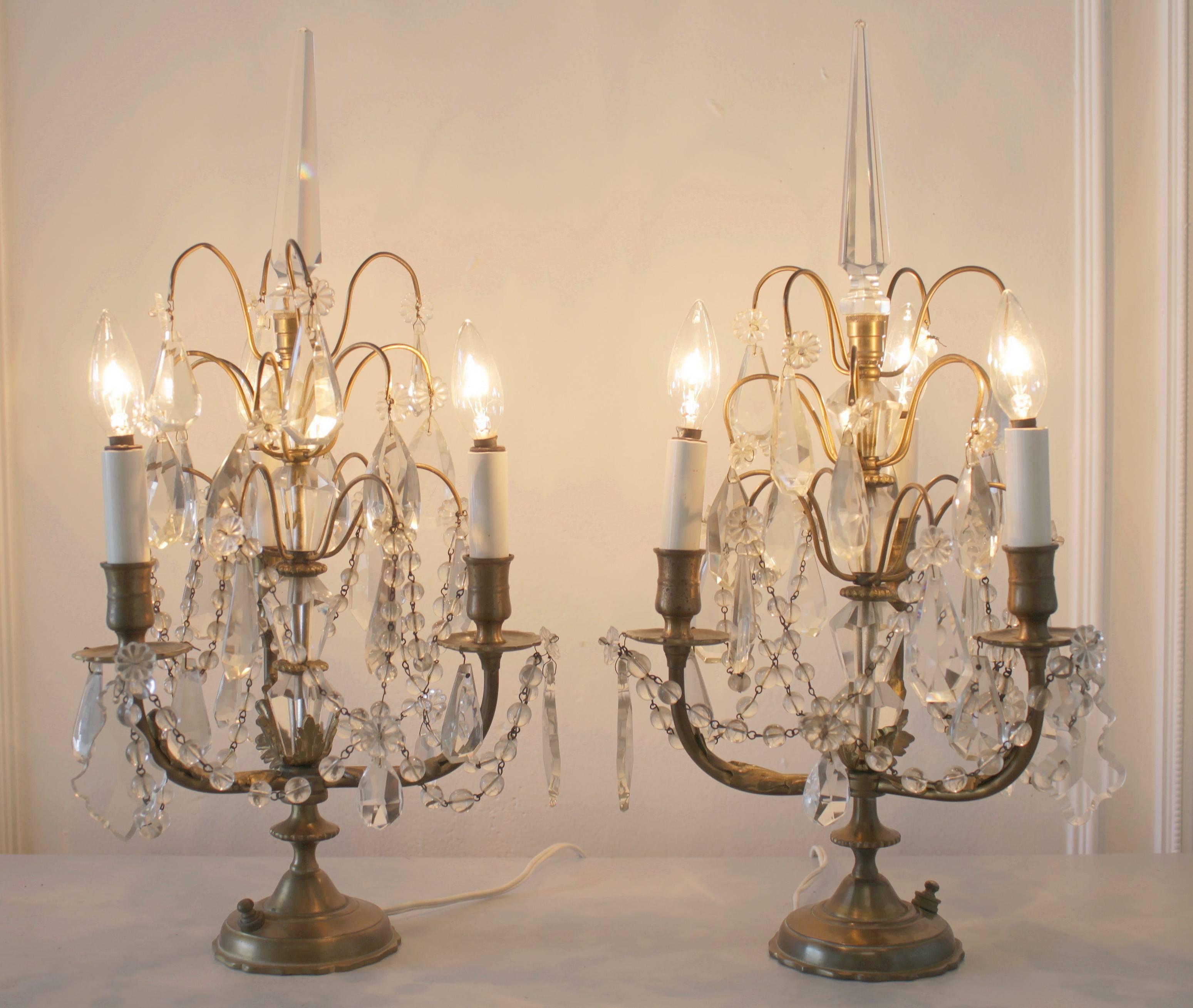 Pair of petite three-light Girandole lamps with swags of English cut beaded crystals and large crystal obelisk. The lamps can be turned on and off easily at the base. They are in good working order and can use 40 watt US chandelier bulbs in each