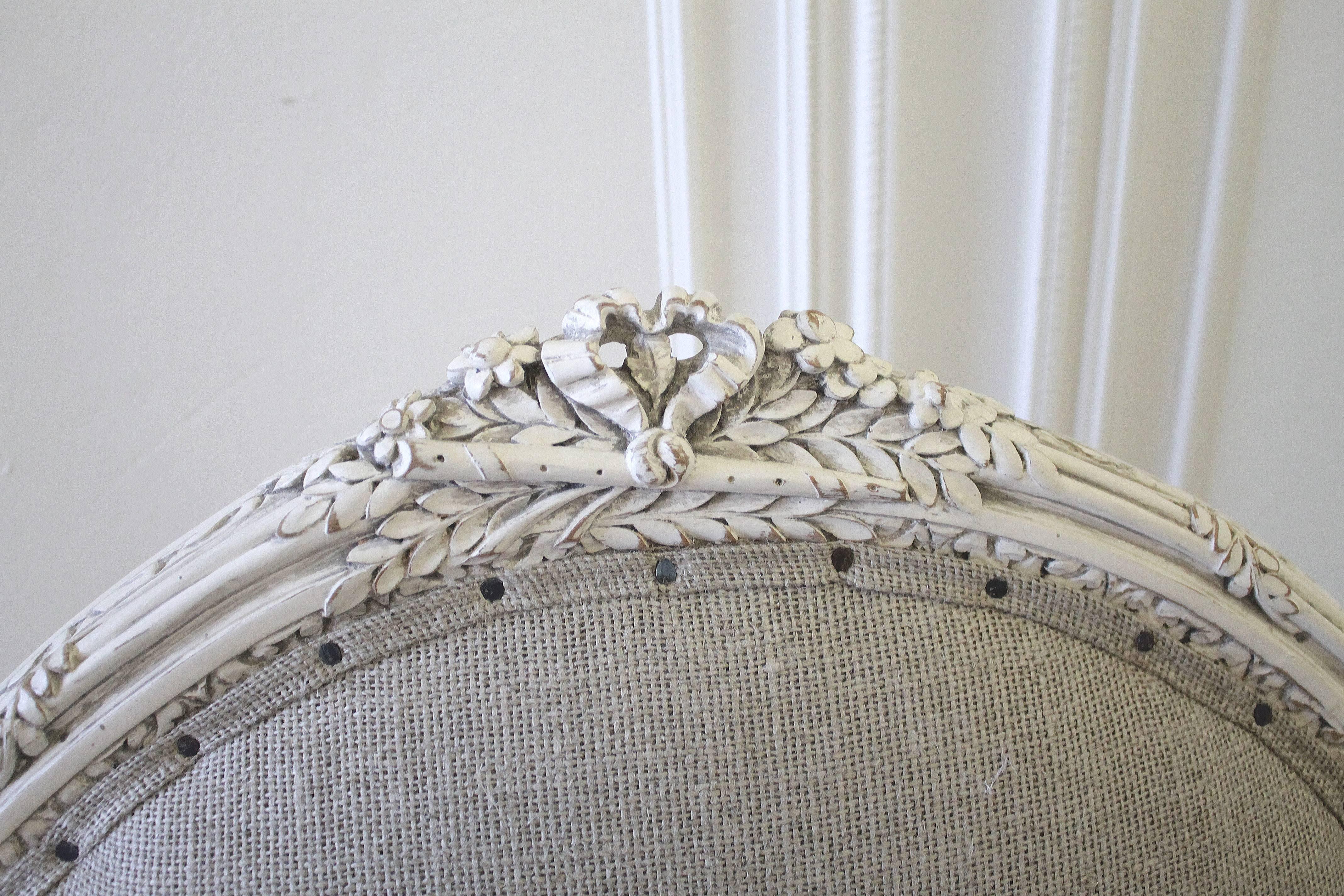 French Louis XVI style arm chair, with a beautiful ribbon, and floral carvings and painted in a soft white, with subtle distressing, and an antique glazed finish, we reupholstered these in our 18oz nubby 100% organic Irish linen. Finished with