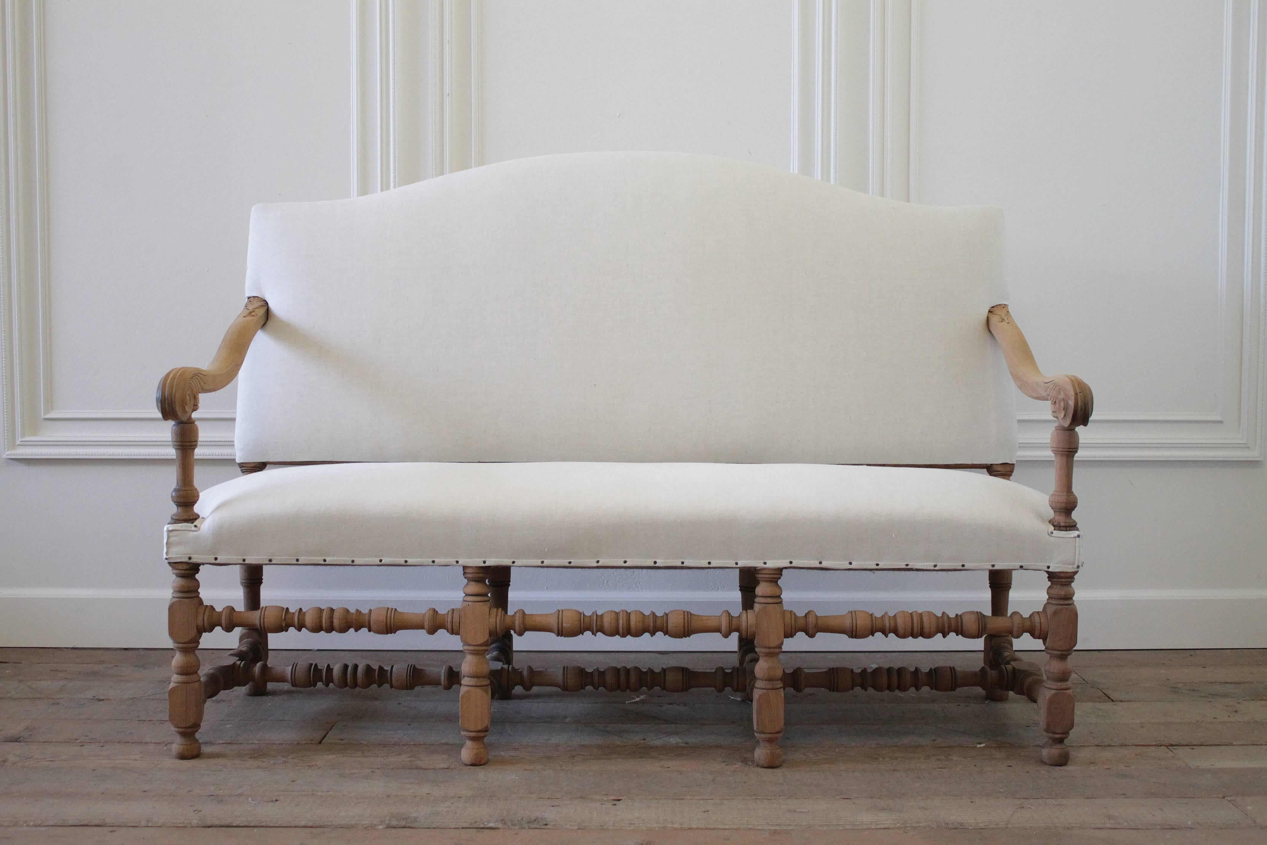 Beautiful carved walnut bench, with a raw stripped finish exposing the natural grains in the wood. We reupholstered this in our organic Belgian linen with an antique nail trim.
Each arm has an oak leaf and acorn carving scrolling down to an