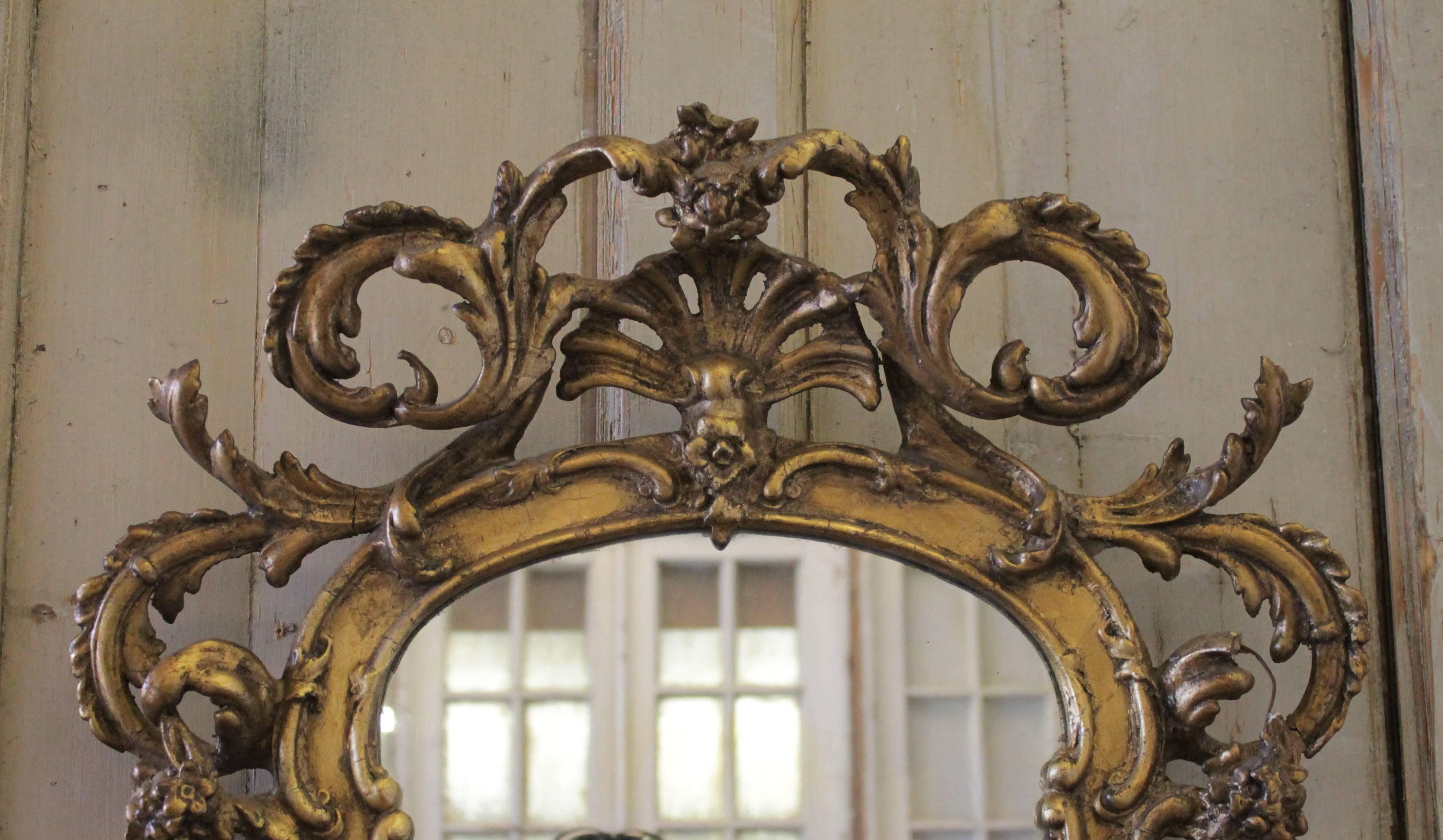 Grand 18th century French giltwood mirrors with scrolls and girandoles. These mirrors have the original mirror with subtle aging. You can see in the reflection of one photo, the small age spots. Made from wood and gesso, the mirror does have some