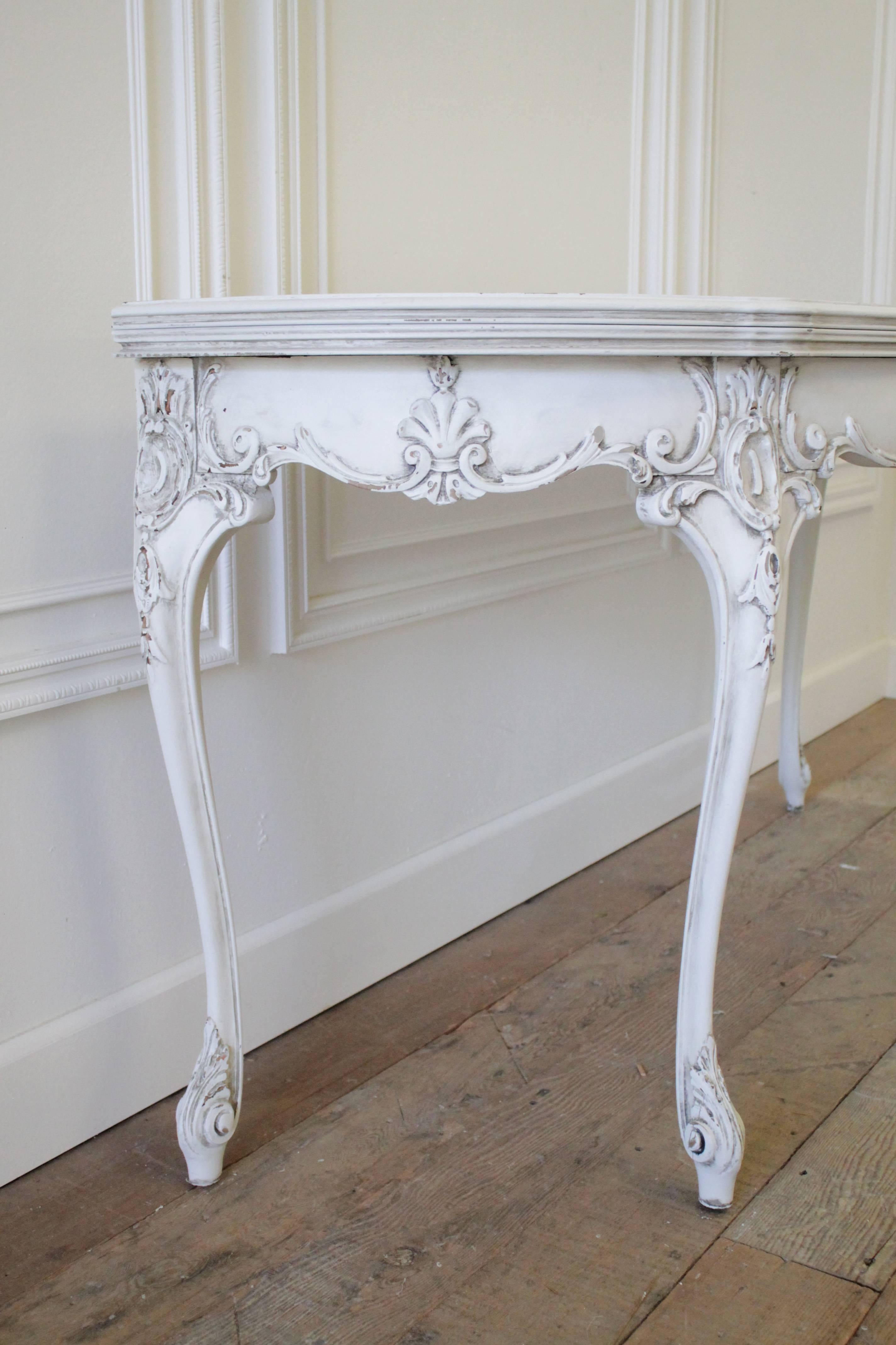 Lovely carved console in the Louis XV style is finished in our oyster white, with subtle distressing, and antique glaze patina. The table top does flip open to be used as a game table or small dining table.
Measures: 60