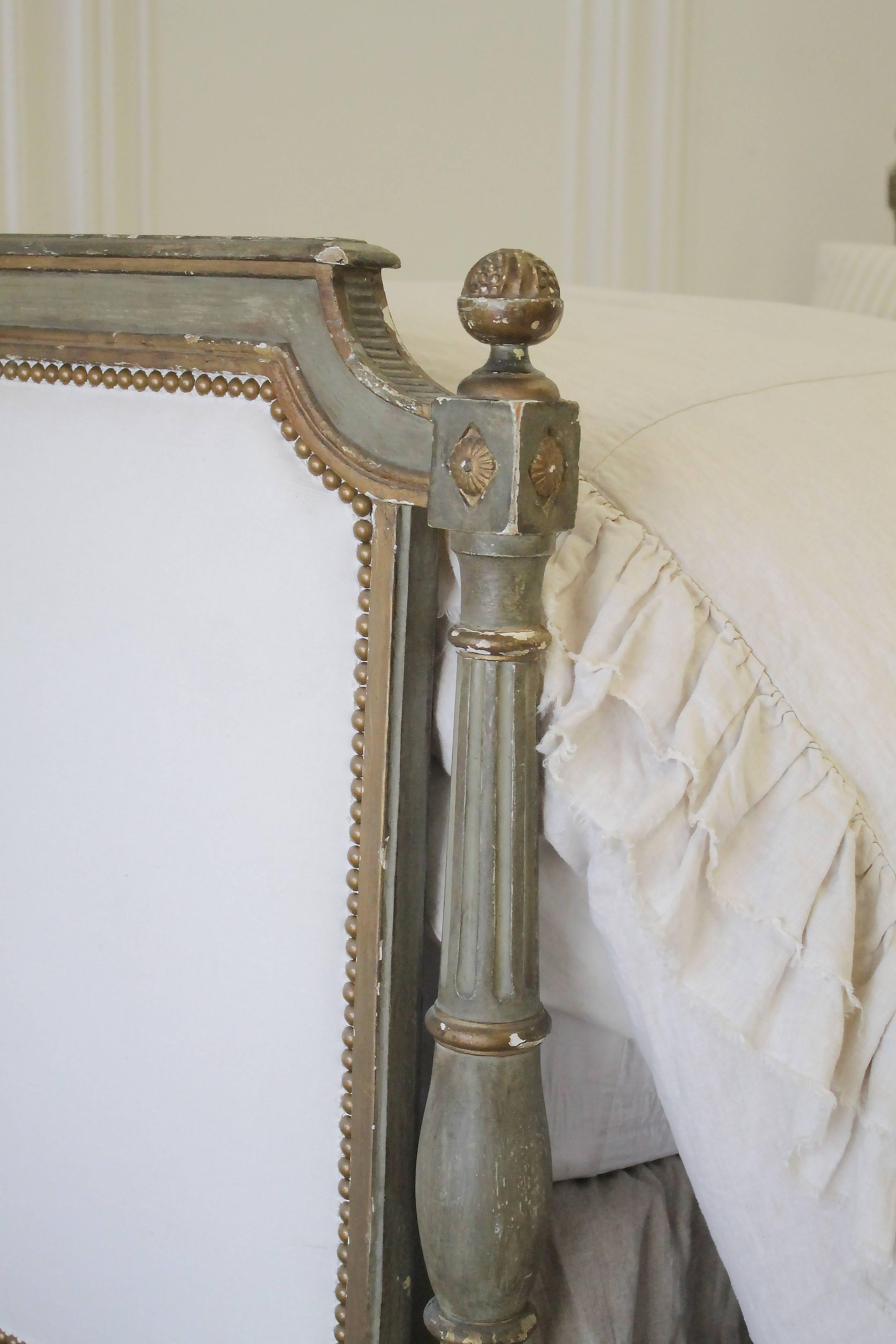 Lovely original painted Louis XVI twin bed, with white cotton upholstery and antique bronze nailhead trim. The painted finish is a muted green with grey hues, and gilded accents. This bed has wonderful patina, perfectly chippy with white peeking