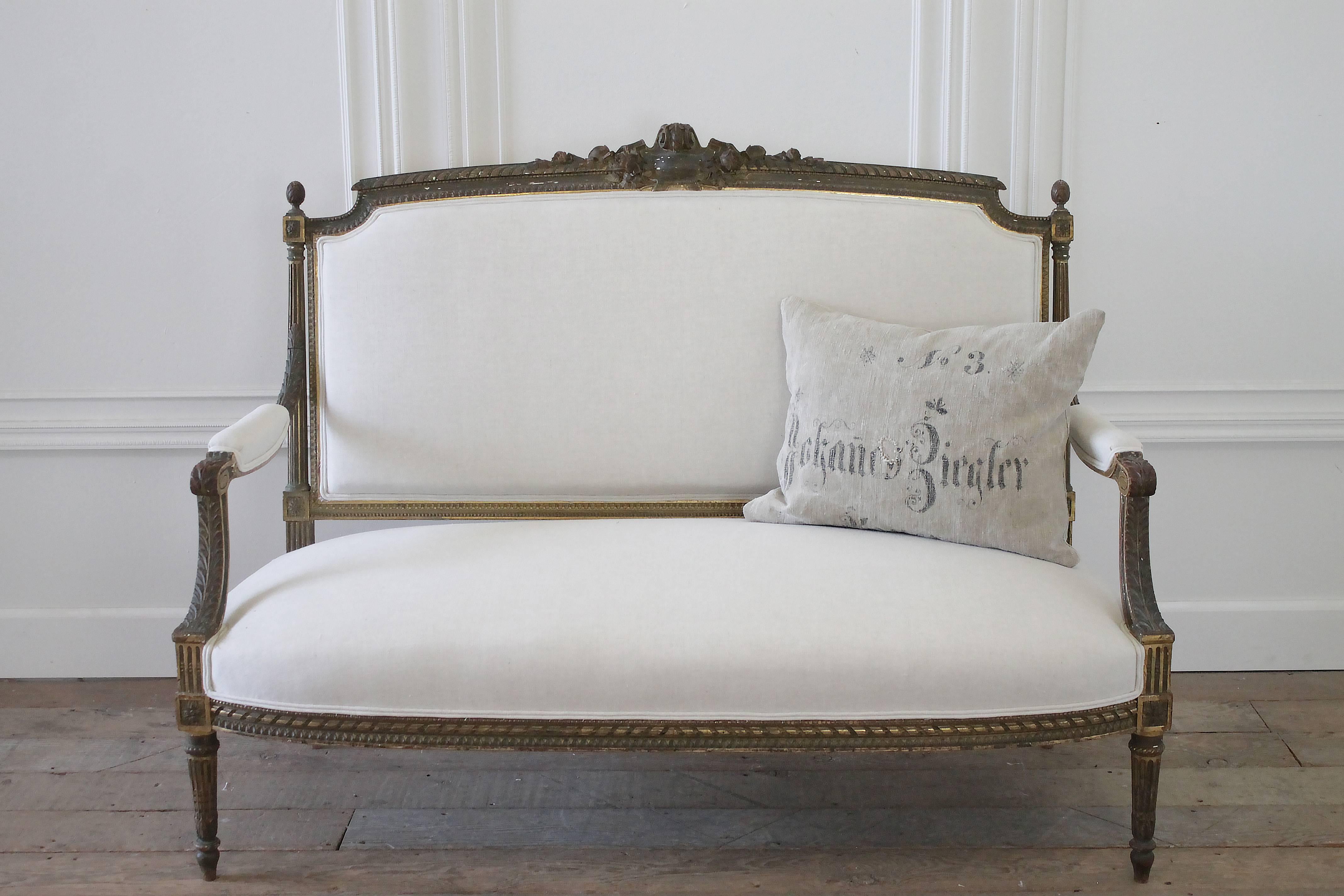 Fabulous settee with original bronze colored gilt finish. A large carved medallion with roses and ribbon details rest atop the back, with small fluted arms and acorn finial. Classic Louis XVI style settee has been reupholstered in our organic