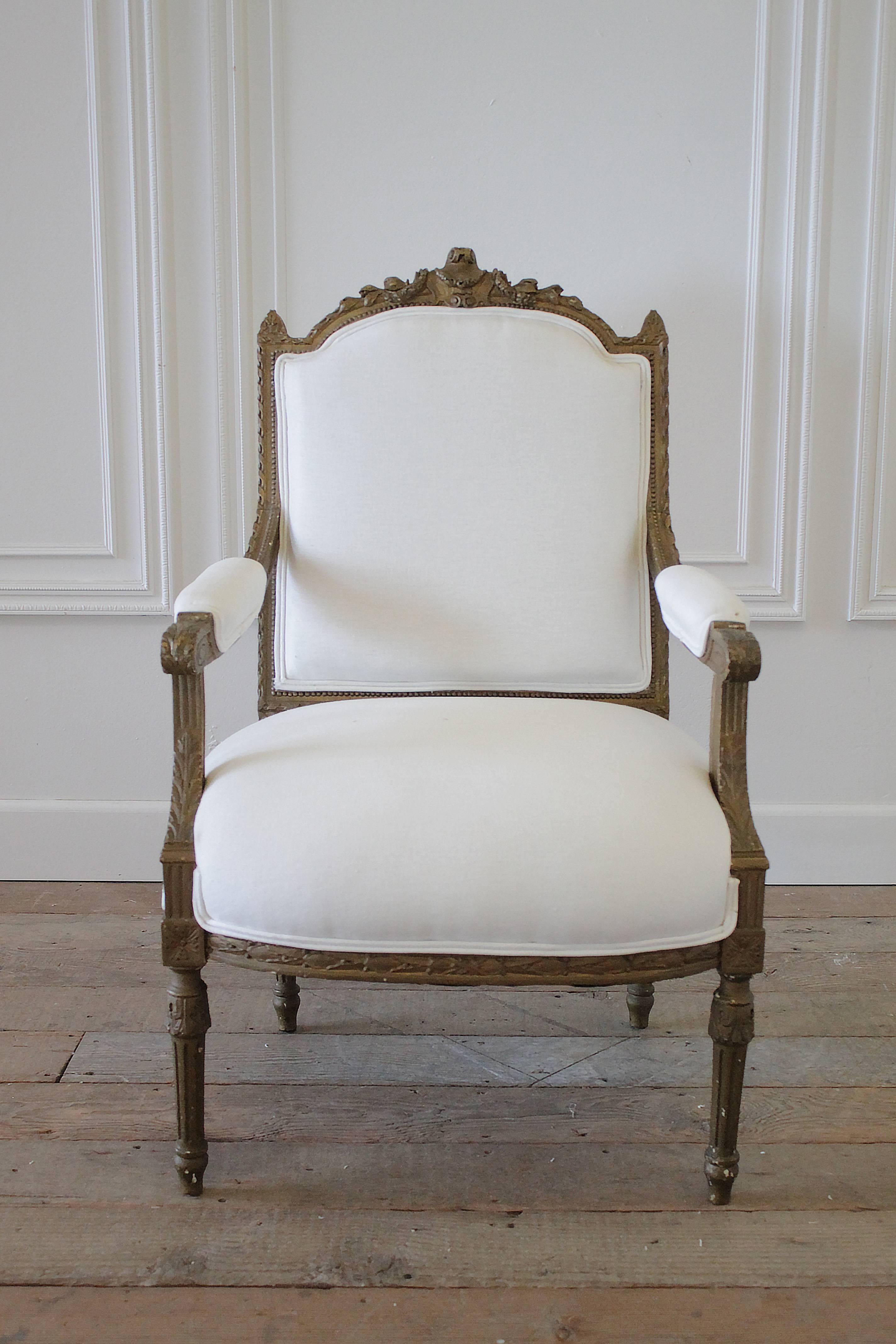 19th century carved open armchair has the original gilt finish, subtle distressing to the gilt with carved sheild medallion, floral swags and curled ribbon edge. The chair has new upholstery in a soft white linen finished with a double