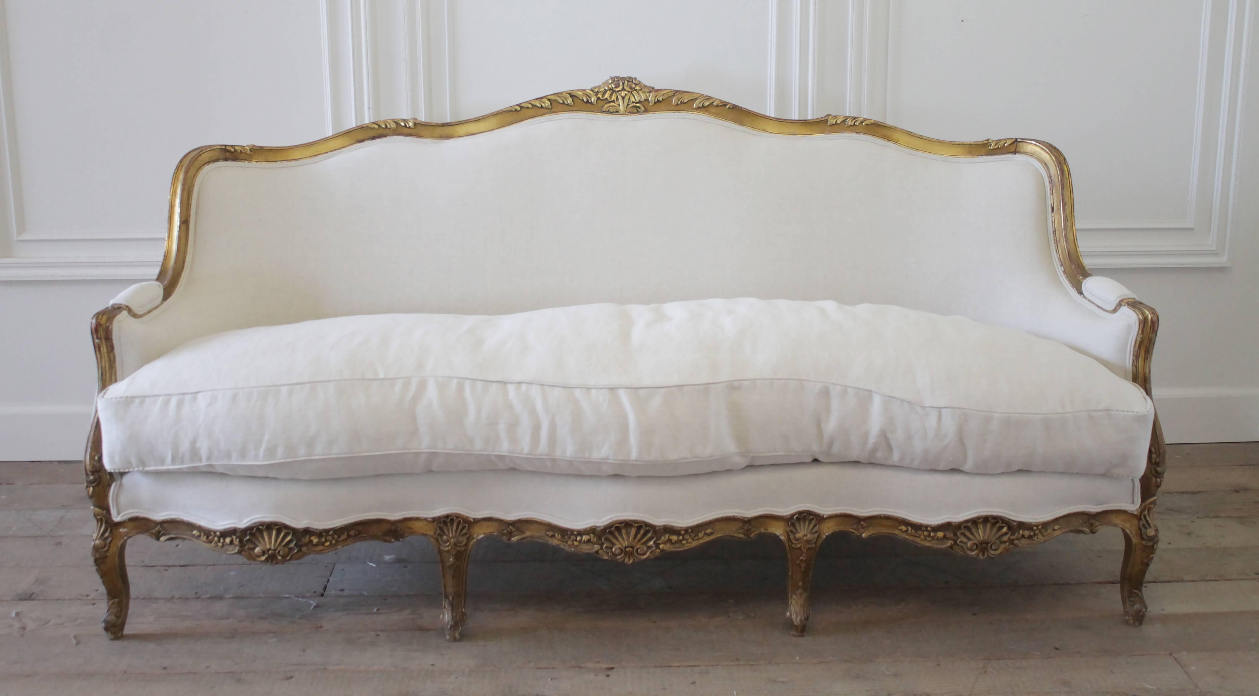 A beautiful giltwood Rococo style sofa has been reupholstered in our 100% organic Belgian linen, and we also added a plump down wrapped cloud cushion slip covered with a flange and pleated ruffle edge. Carved shells and roses, with trailing leaves