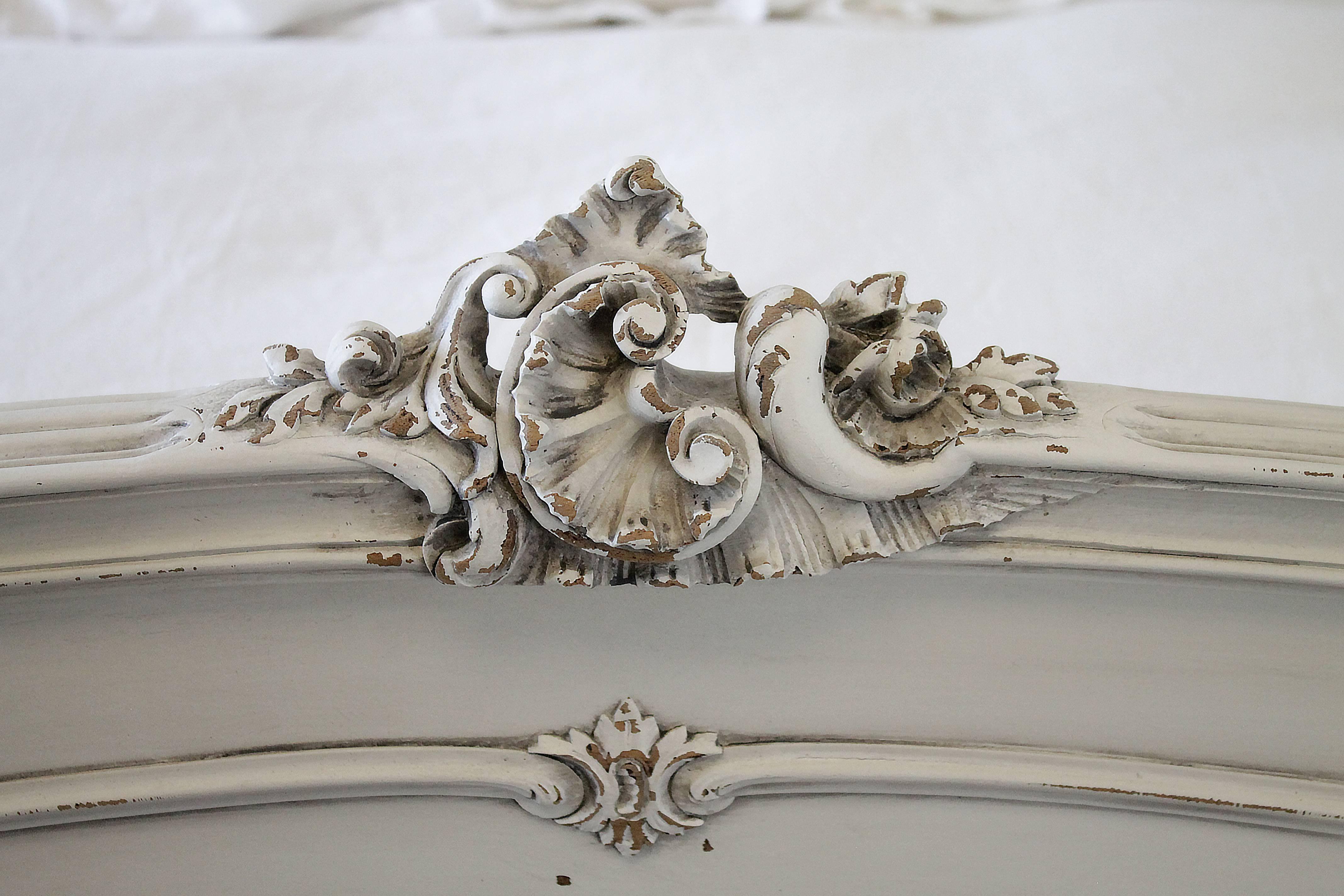 Antique French bed in the Louis XV style has been painted in a soft oyster white color, with subtle distressing and an antique glaze finish. A large beautiful carved cartouche with roses on both headboard and footboard.
Original side rails are