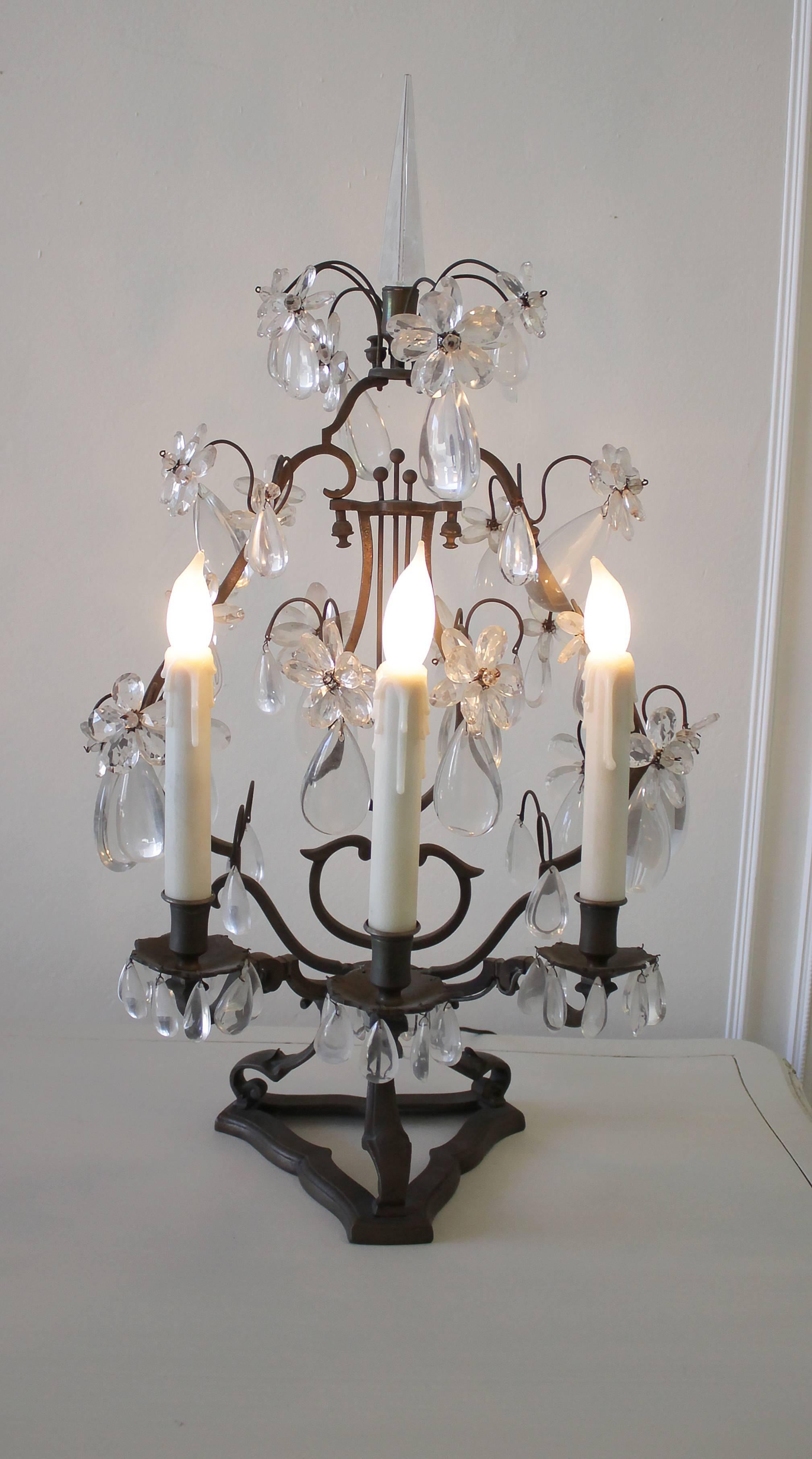 19th century bronze and crystal girandole from France. Ornately cut, tear shaped crystals, each with ten petal floral crystals above, adorn every inch of these candelabras. The frames are made of scrolled bronze resembling a harp, bearing an aged