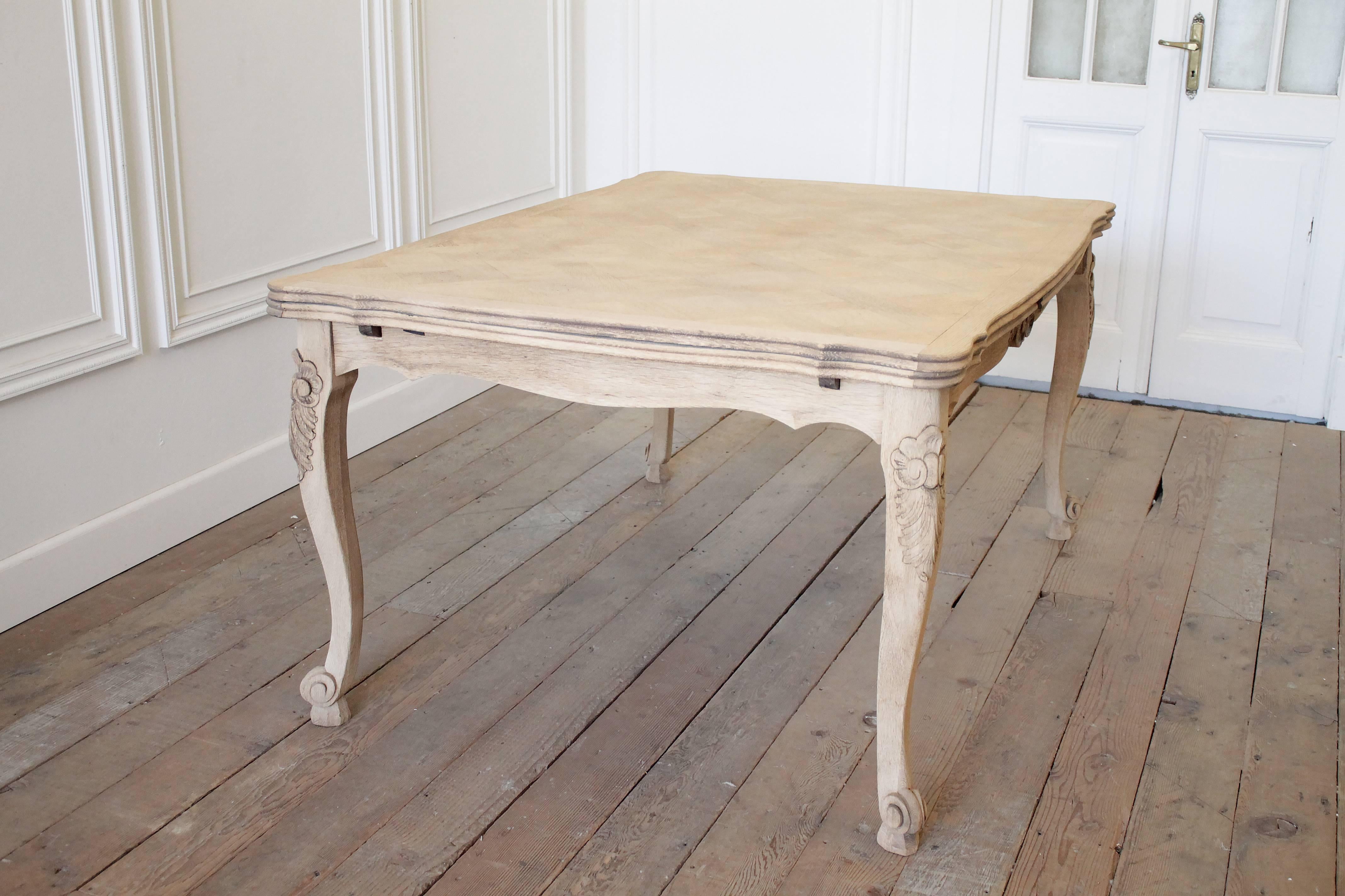 French draw-leaf dining table with a carefully stripped parquet top and painted base. The leaves can be easily drawn out without damaging the finish. Large carved leaf and clam shell design on four legs and apron. 

The table fully extended is