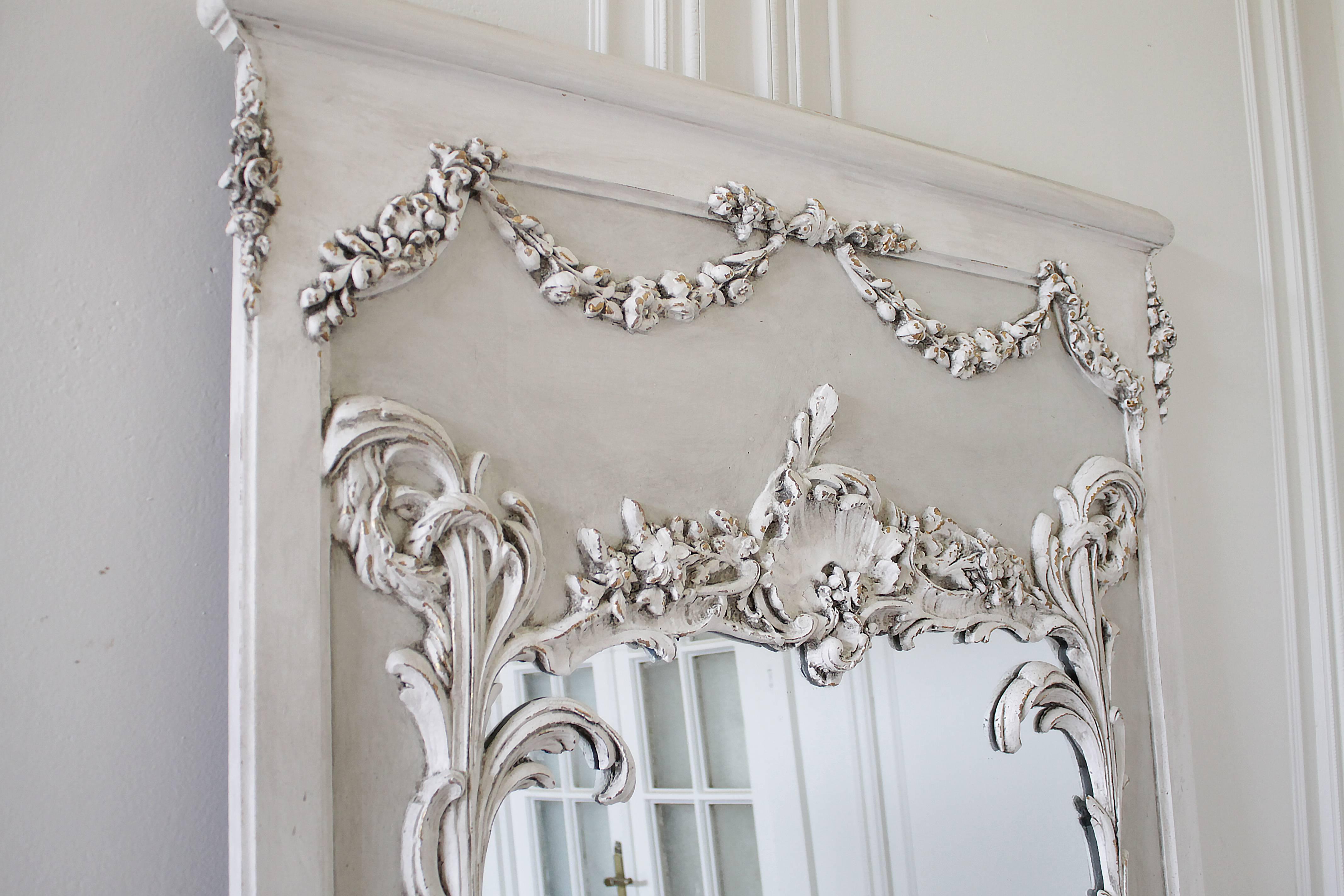 Fabulous pair of French mirrors with large carved cartouche, and floral swags, and trailing vines. Finished in our two-tone painted oyster white, with subtle distressing, and antique patina. Sold individually, these large trumeau mirrors are great