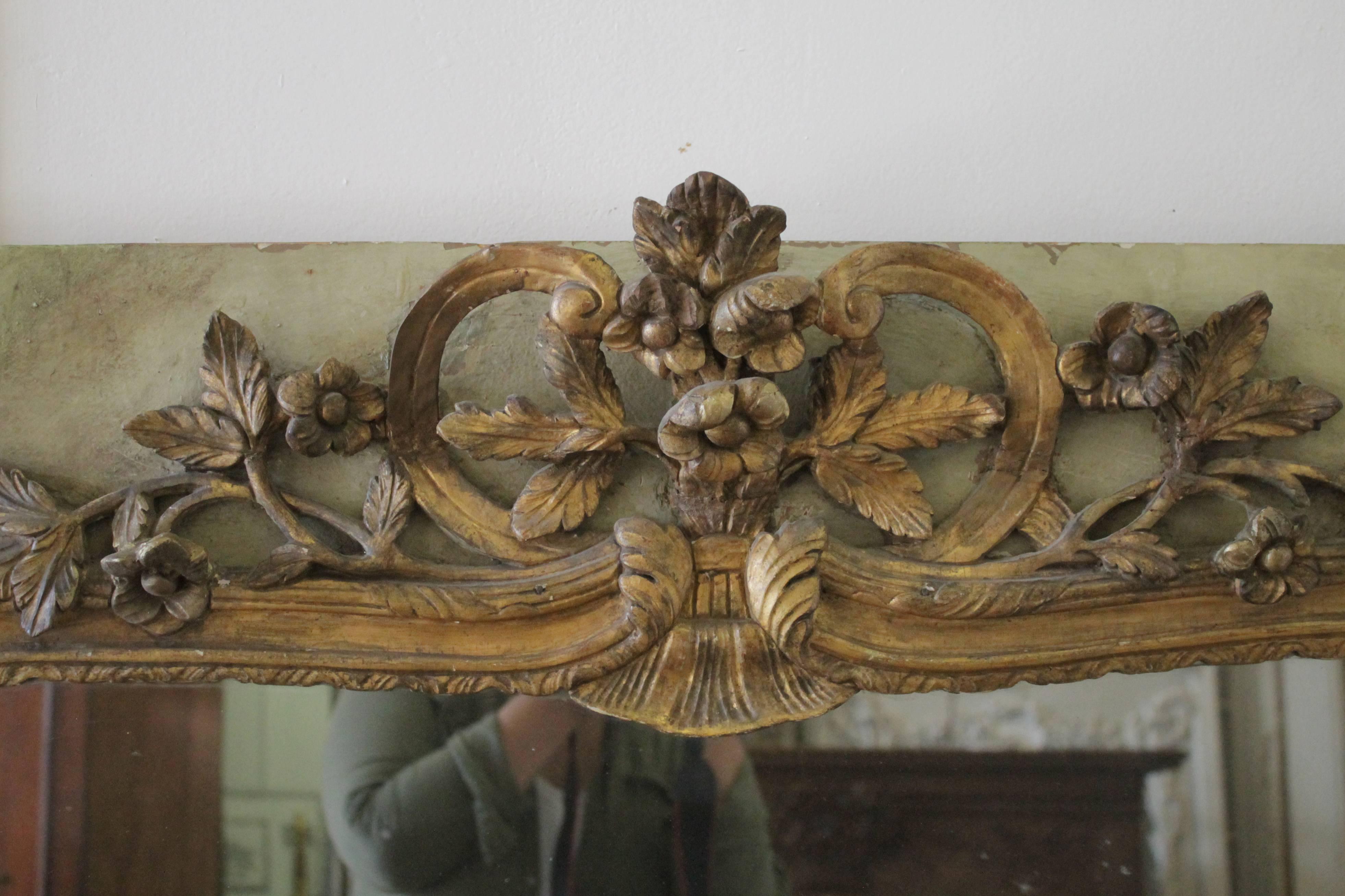 Gorgeous French trumeau with large carved roses and vines in a faded patina gilt finish. The wood frame has the original paint finish in a soft sage with creamy tones showing through. The mirror is original with signs of age, with fading, and dark