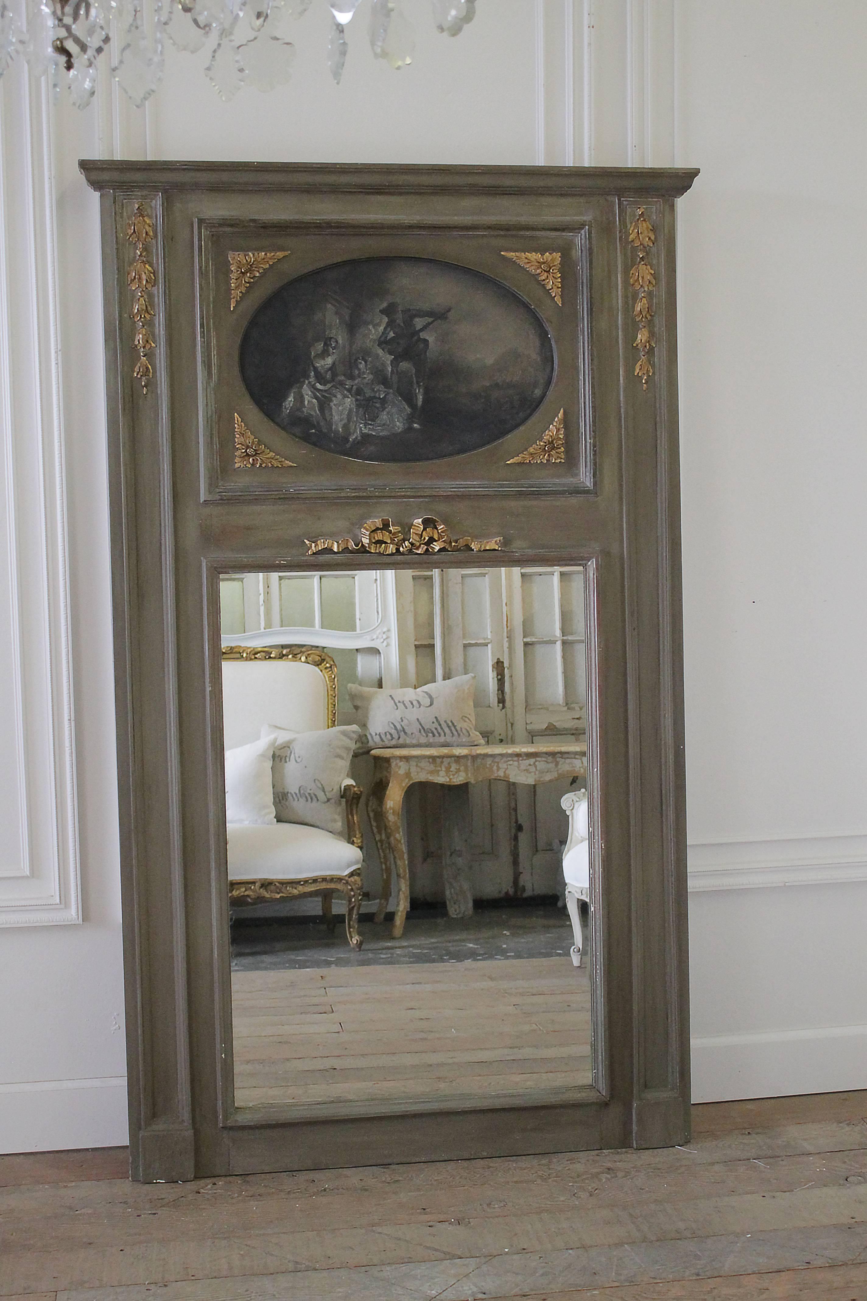 An early 20th century French pier mirror or trumeau, painted in a weathered grey tone and gilded, with oil on canvas picture inset at top in oval gilded frame with bow.
Measures: 44.5