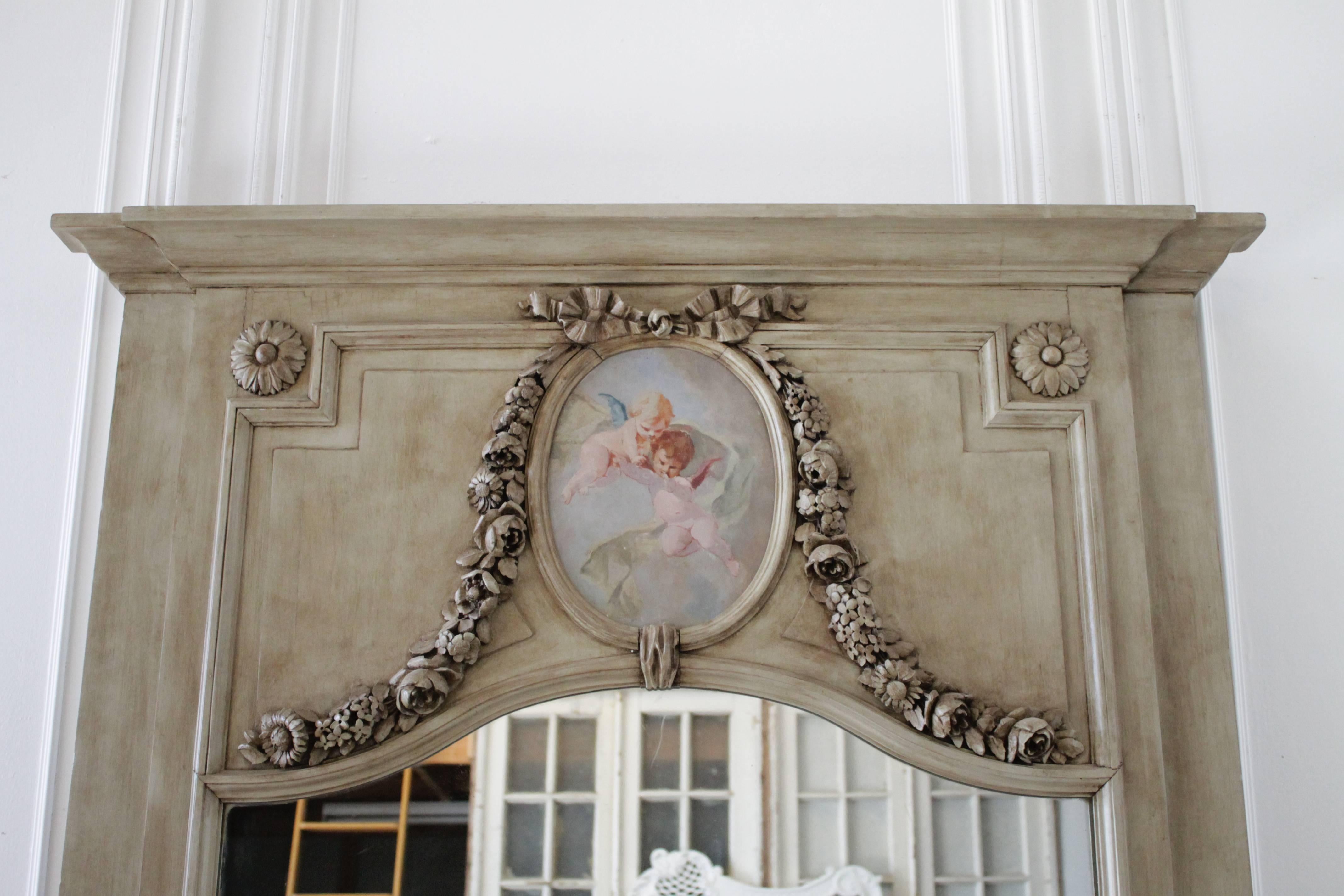 Beautiful large trumeau in the French Style, with hand-painted cherub scene. A large carved ribbon and rose swags add a romantic touch to this simple frame.
Original beveled mirror.
Measures: 51.5