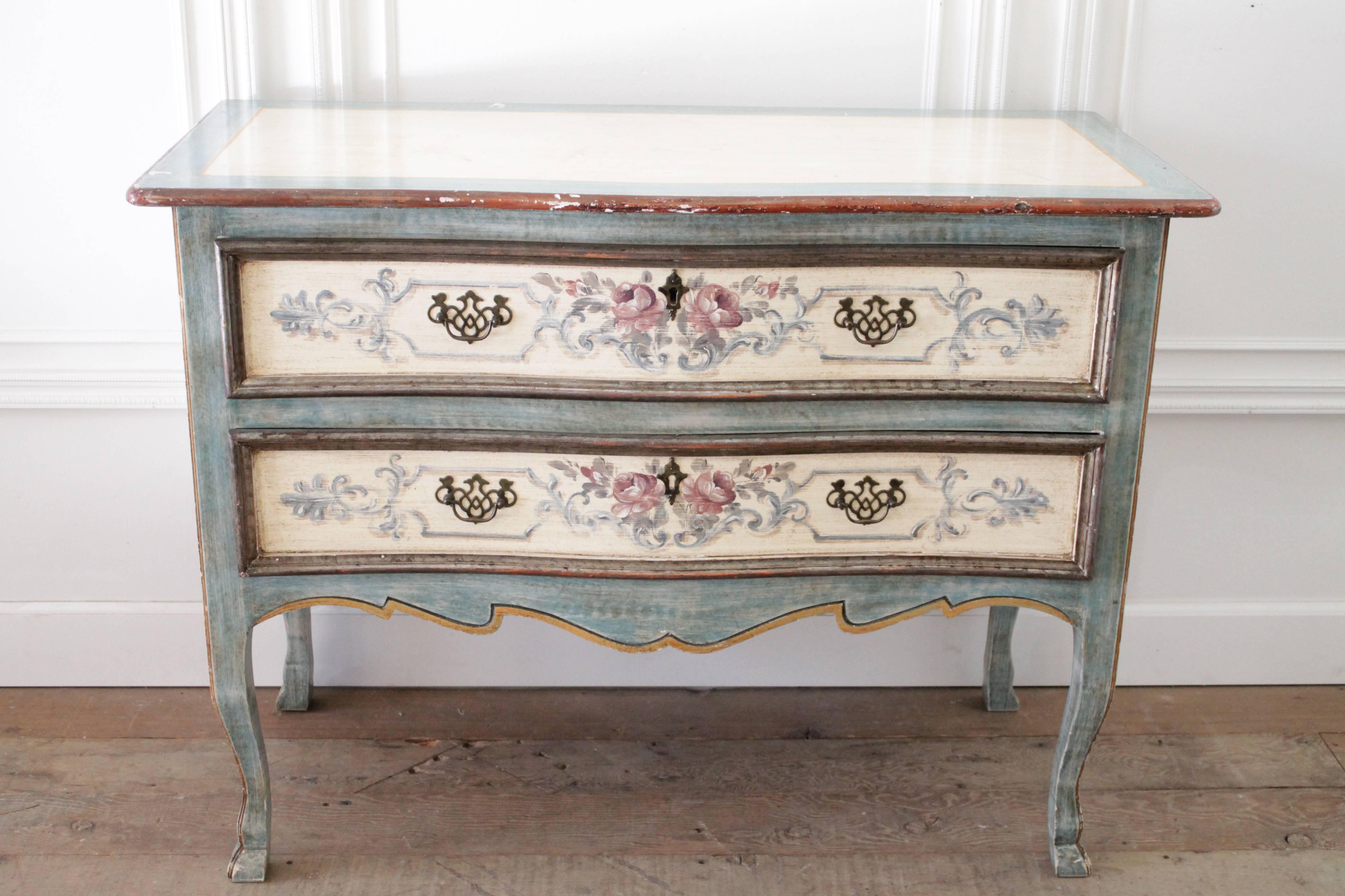 Lovely two-drawer Italian commode painted in a soft pale aqua, and cream color. Hand-painted floral details on the drawers, with iron pulls.
Has an aged distressed paint patina, with chips or scuff on edges. Legs are sturdy, drawers open and close