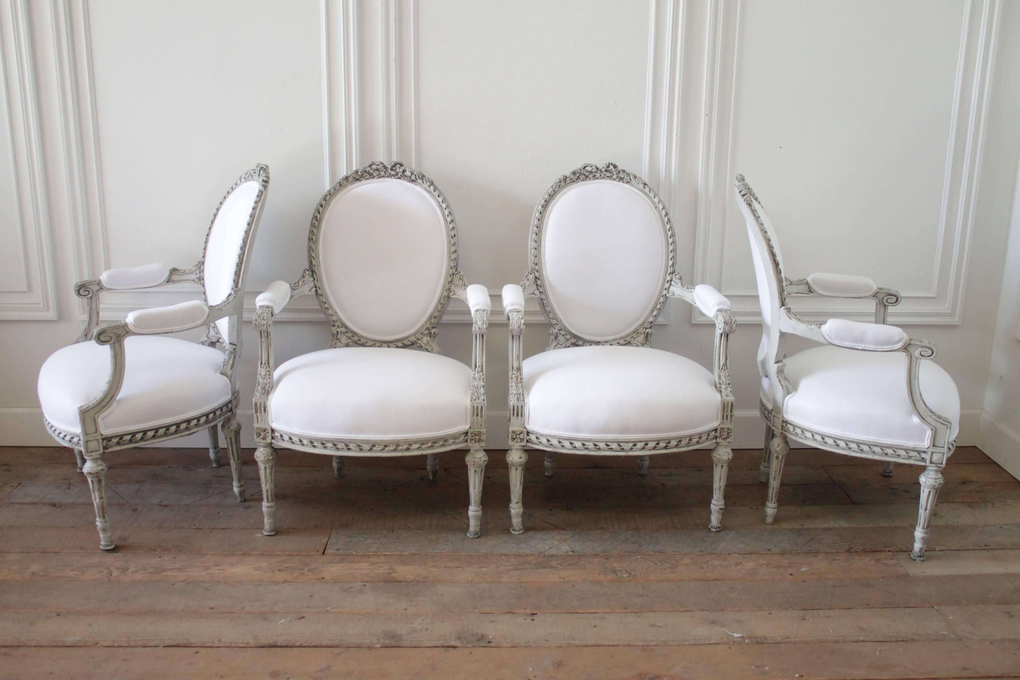Lovely Louis XVI carved ribbons chairs we have reupholstered in a soft washed white organic Belgian linen. The frames are painted in our custom French grey antique finish. Subtle tones of original gilt and white are peeking through the distressed