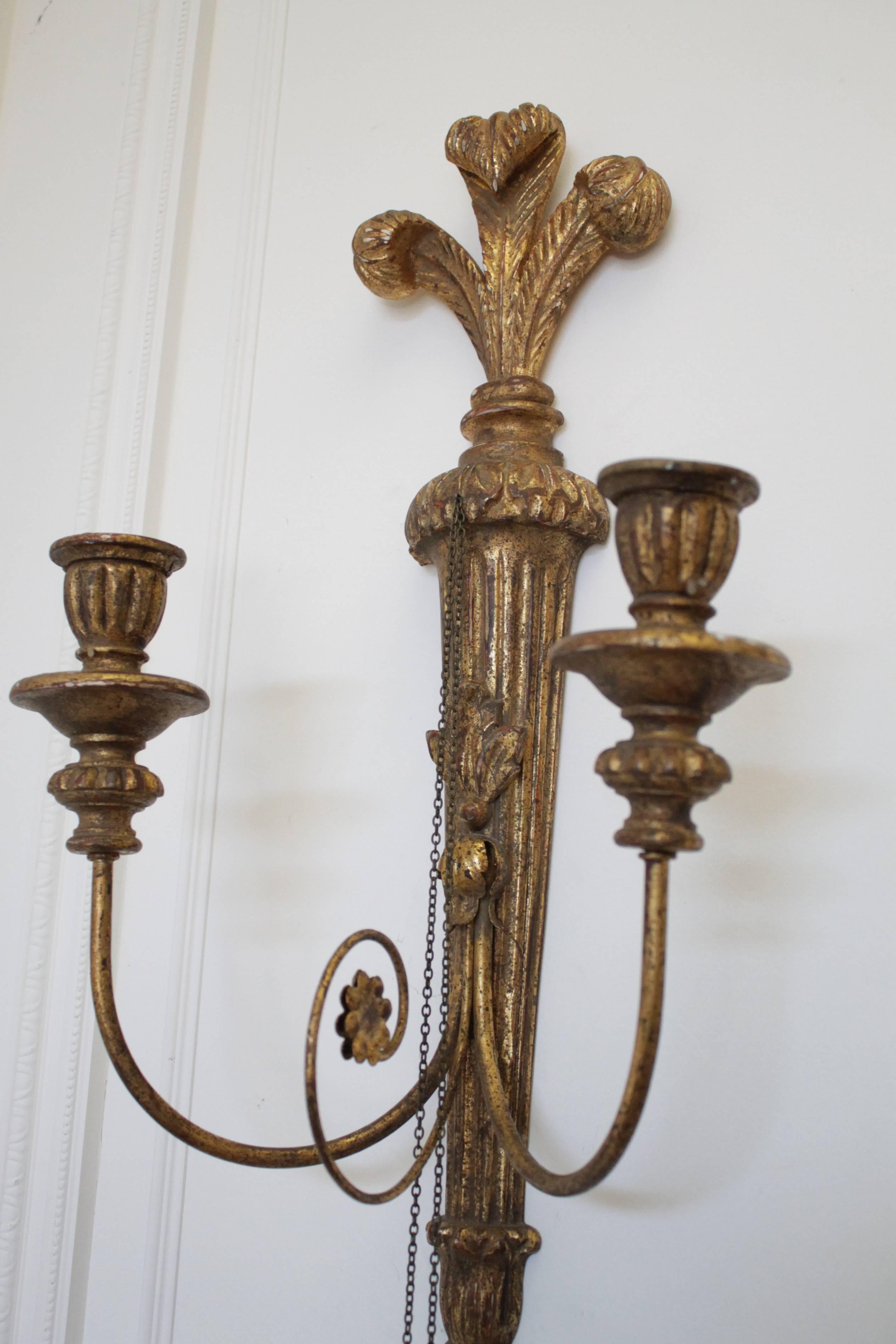 Nicely carved wood sconces made to hold candles, made in Italy. The arms are iron, with wood candle bases, and the tassels hang from a small looped chain. On the back stamped 