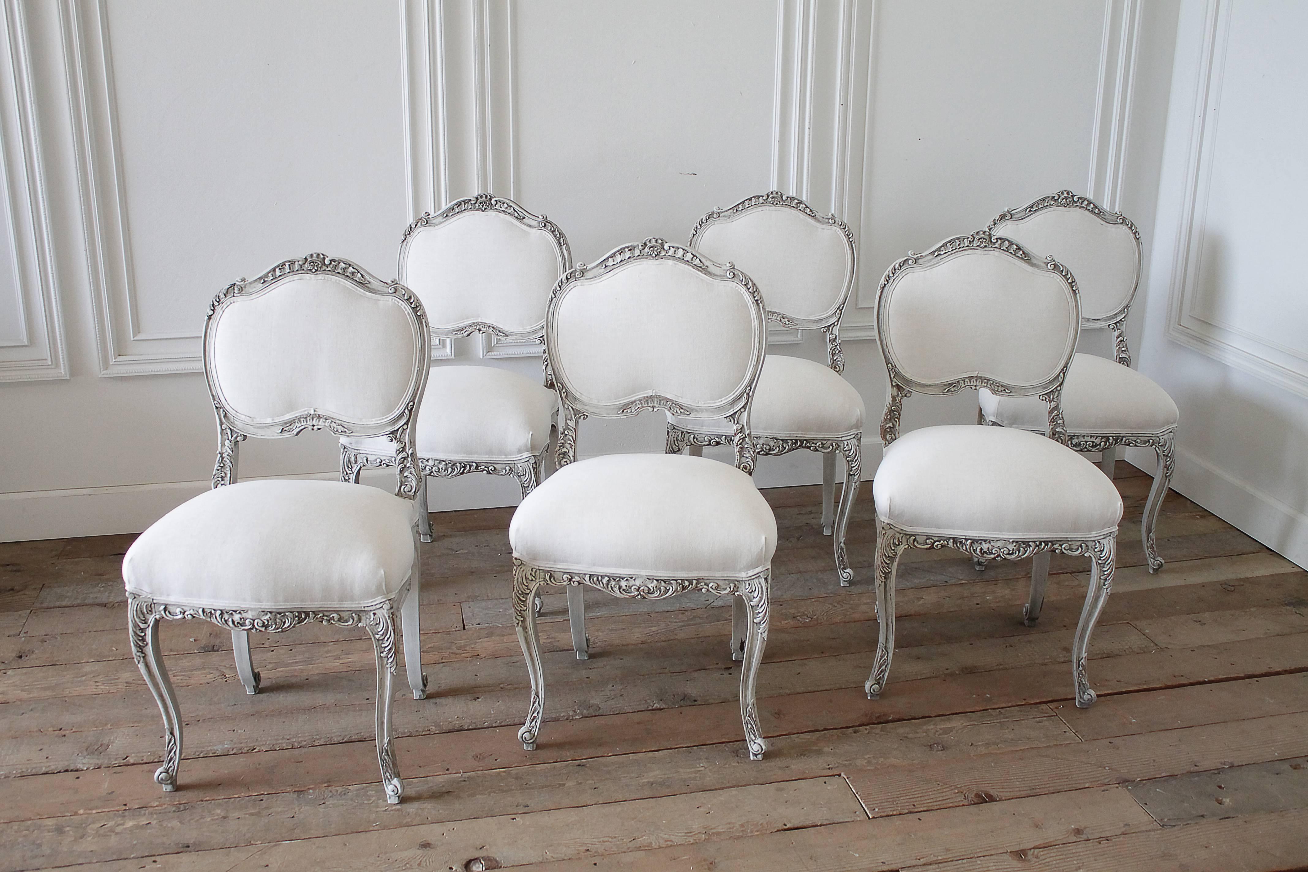 Lovely set of 6 dining chairs, solid hard wood, painted in a French grey with slight distressing, upholstered in a light oatmeal Belgian linen. Carved French cartouche atop the backs, with curved Louis XV style legs. Seats have springs, comfortable