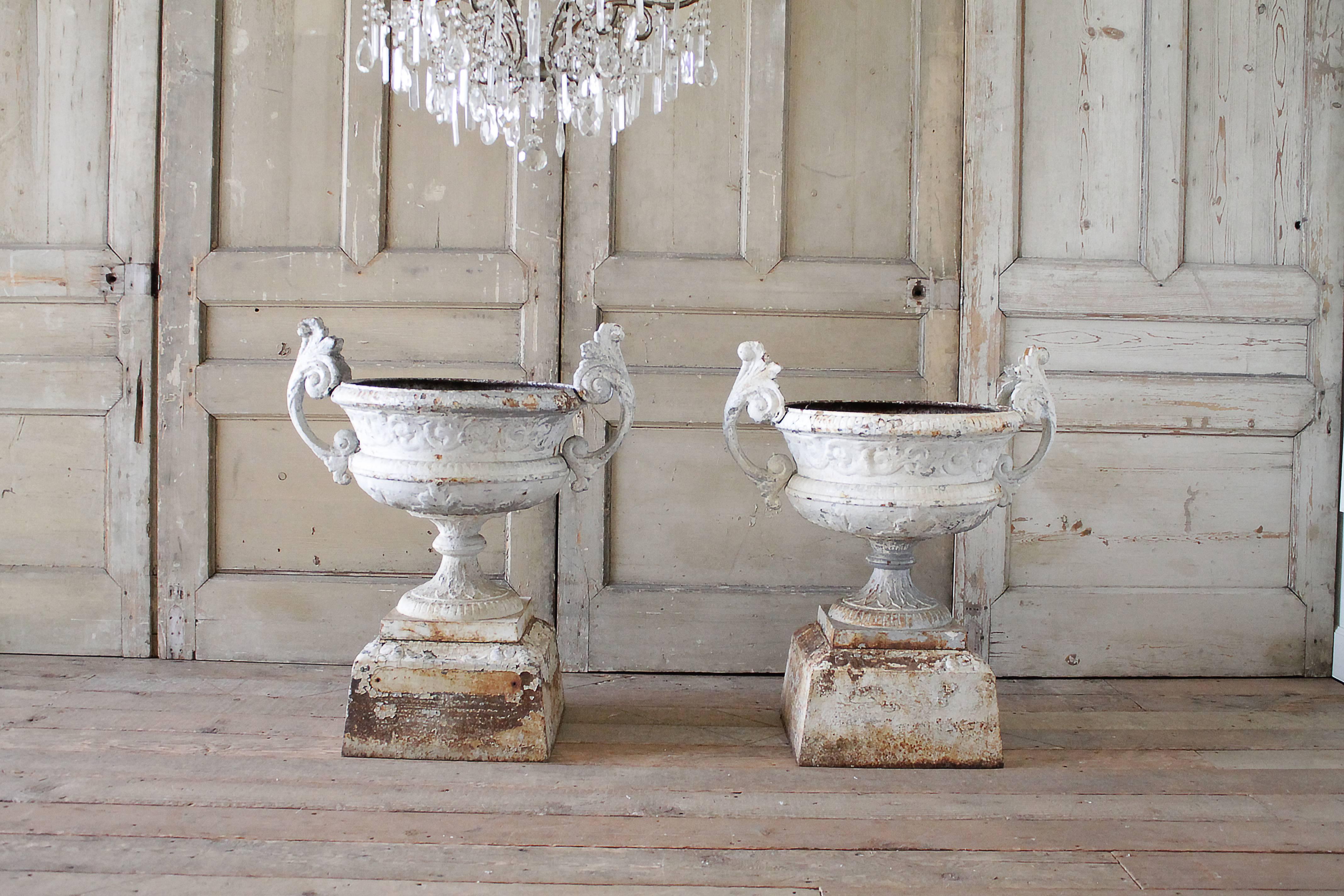 Beautiful pair of cast iron urns with handles. These come apart into three pieces, when stacked they are very sturdy and feel as if they are one piece. Perfectly aged paint peeling and chipping. One urn has a crack, however it is still solid and