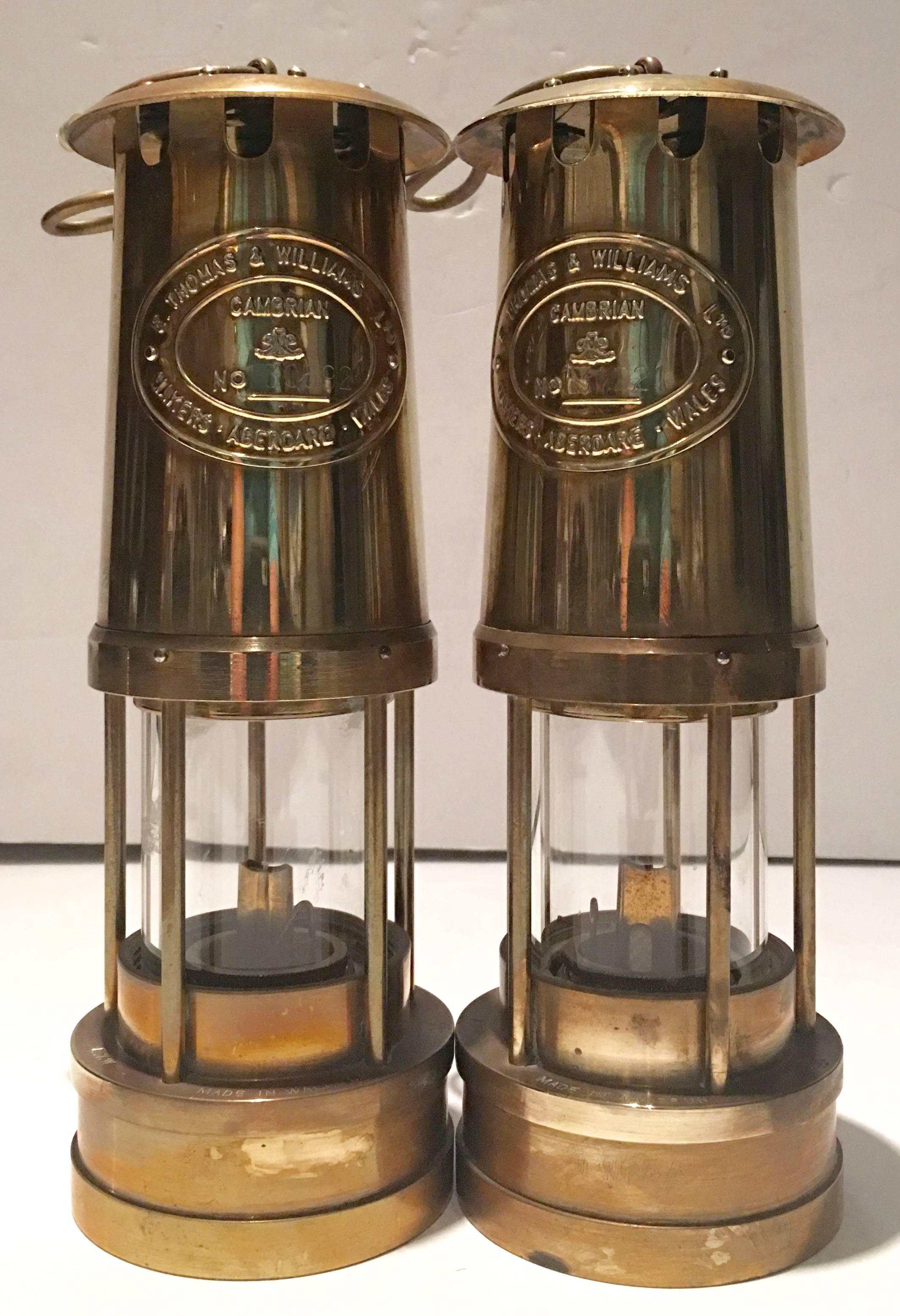 1980s pair of British Cambrian solid brass hanging miners lamps. Each piece has is numbered and dated. Features a milled glass tank with wick. Each lamp includes a solid brass gimbaled wall hook. Can be used as a table lamp or hanging lantern. Each