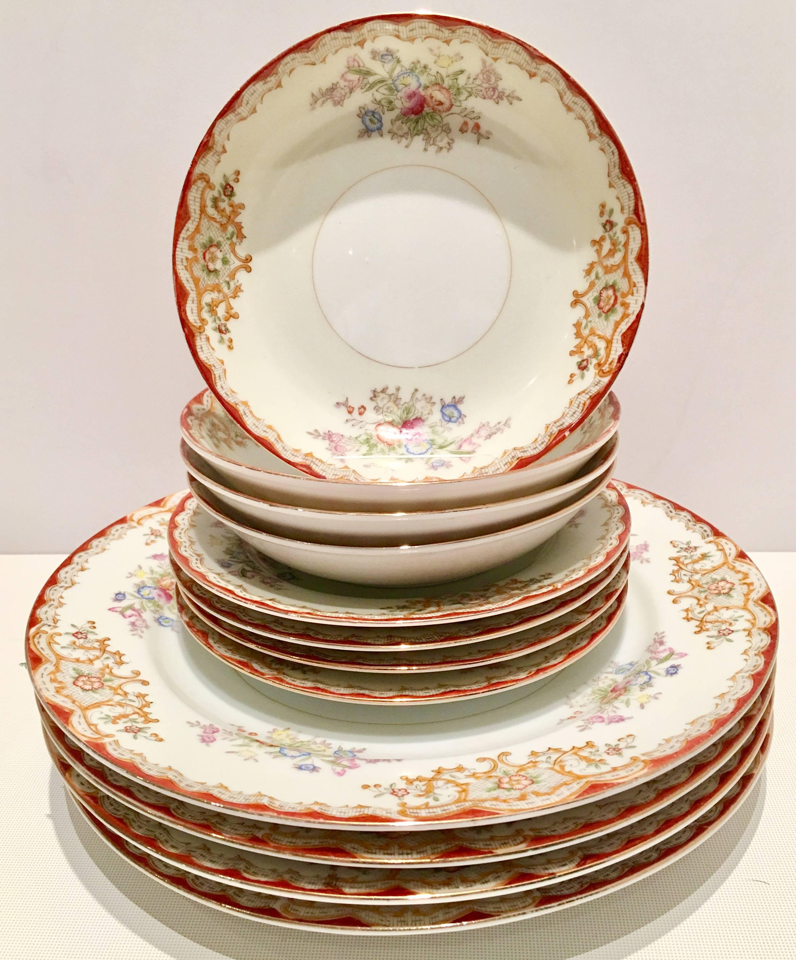 Art Nouveau style Japanese hand-painted porcelain dinnerware set of four “three pieces” settings with 22-karat gold edge detail. Scroll and rose patter of white and cream ground with a red and 22-karat gold edge and bright orange dominating color