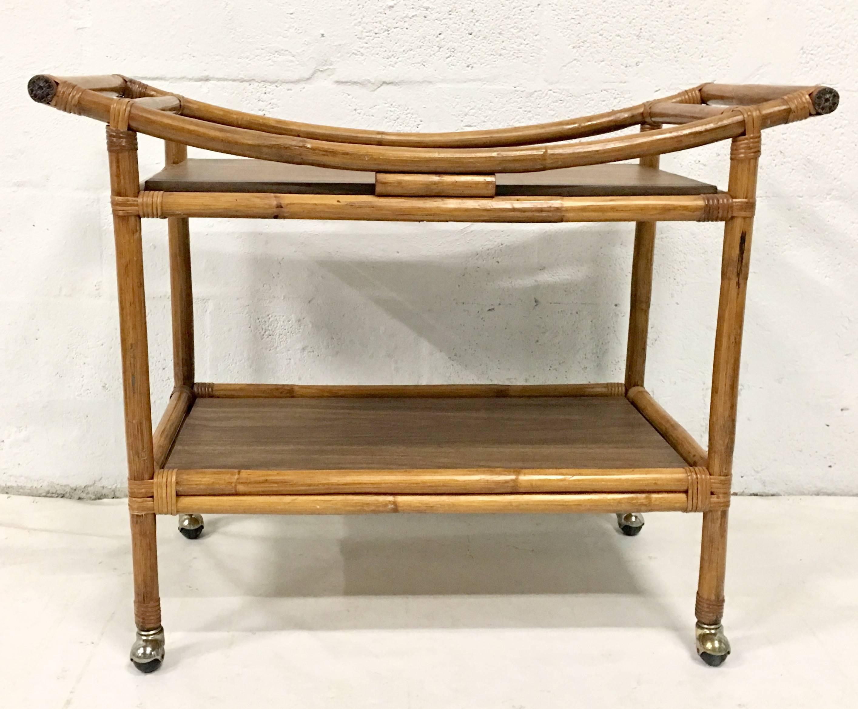1940s Rattan rolling serving cart with original brass capped wheels, faux bois laminate covered particle board and carved end cap handles.