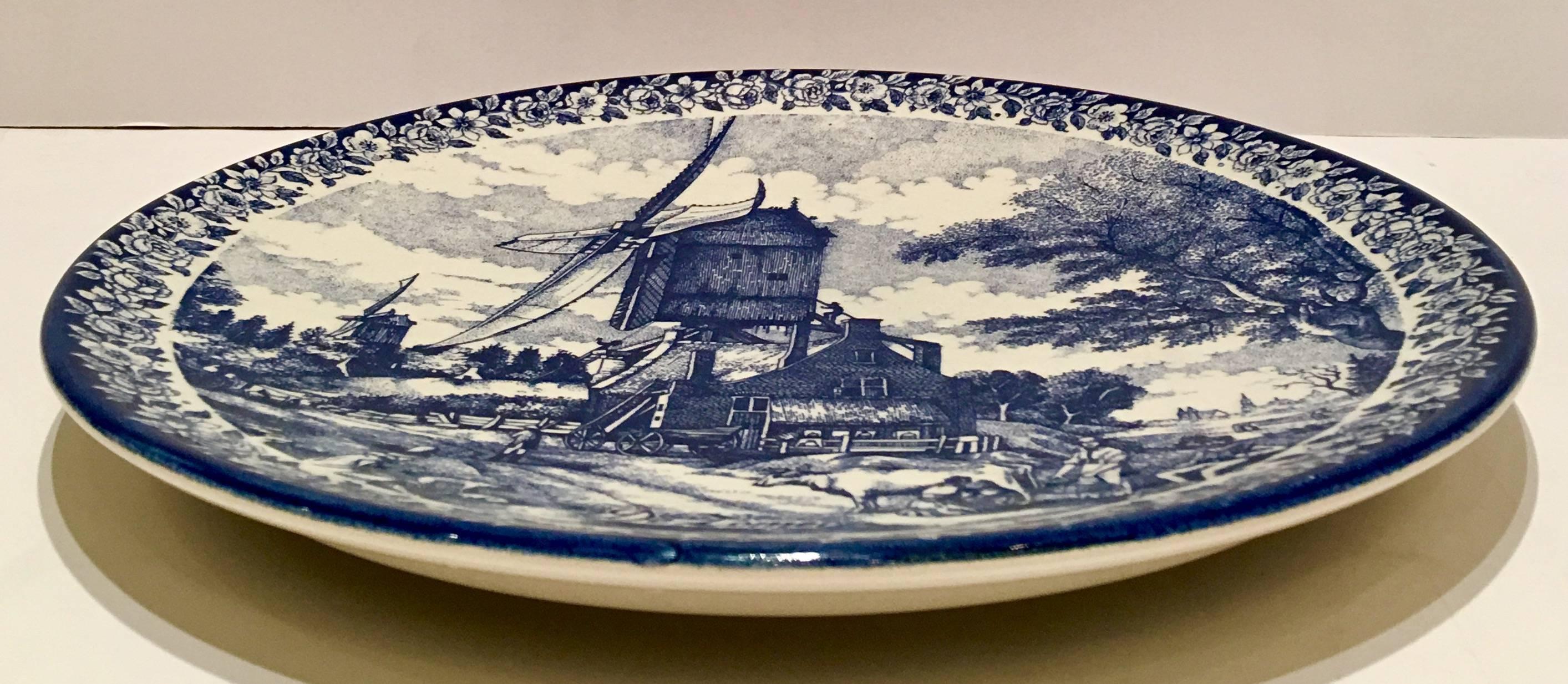 Dutch Delft large blue and white hanging charger plate. Features a farm house and windmill and with a floral vine pattern detail. is titled, 