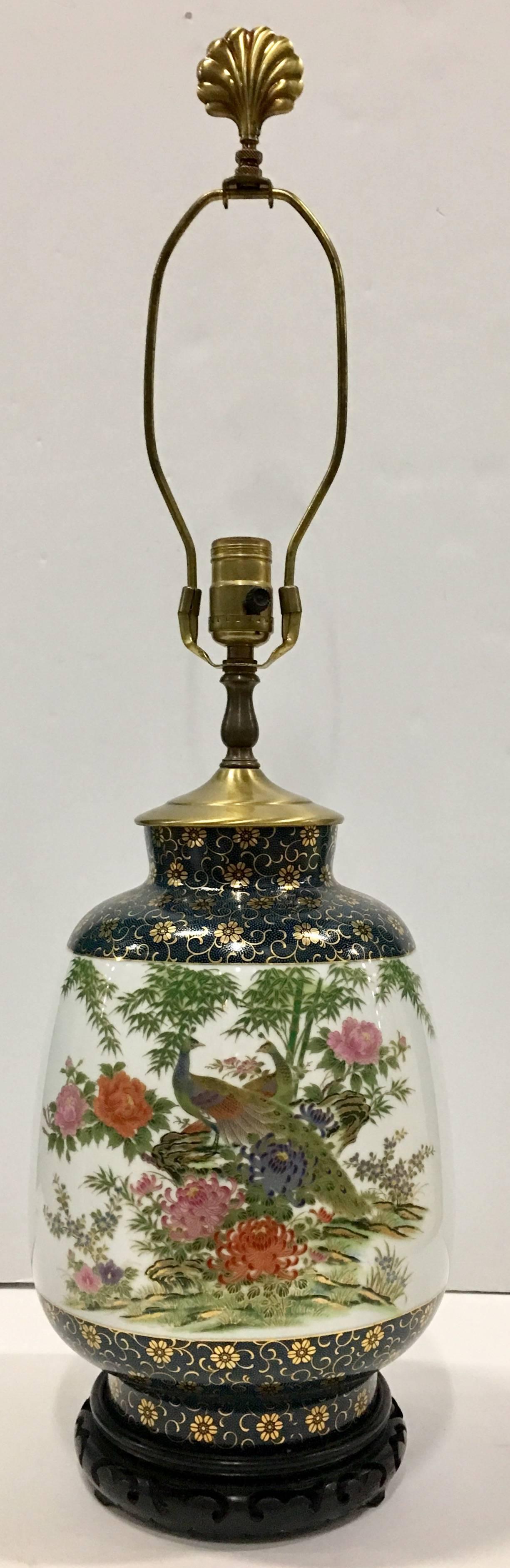 Stunning Asian Style hand-painted with gilt detail peacock motif lamp on rosewood carved base and brass fittings. Includes brass harp and brass shell motif finial. Wired for the US and in working order. Height to socket 19.25