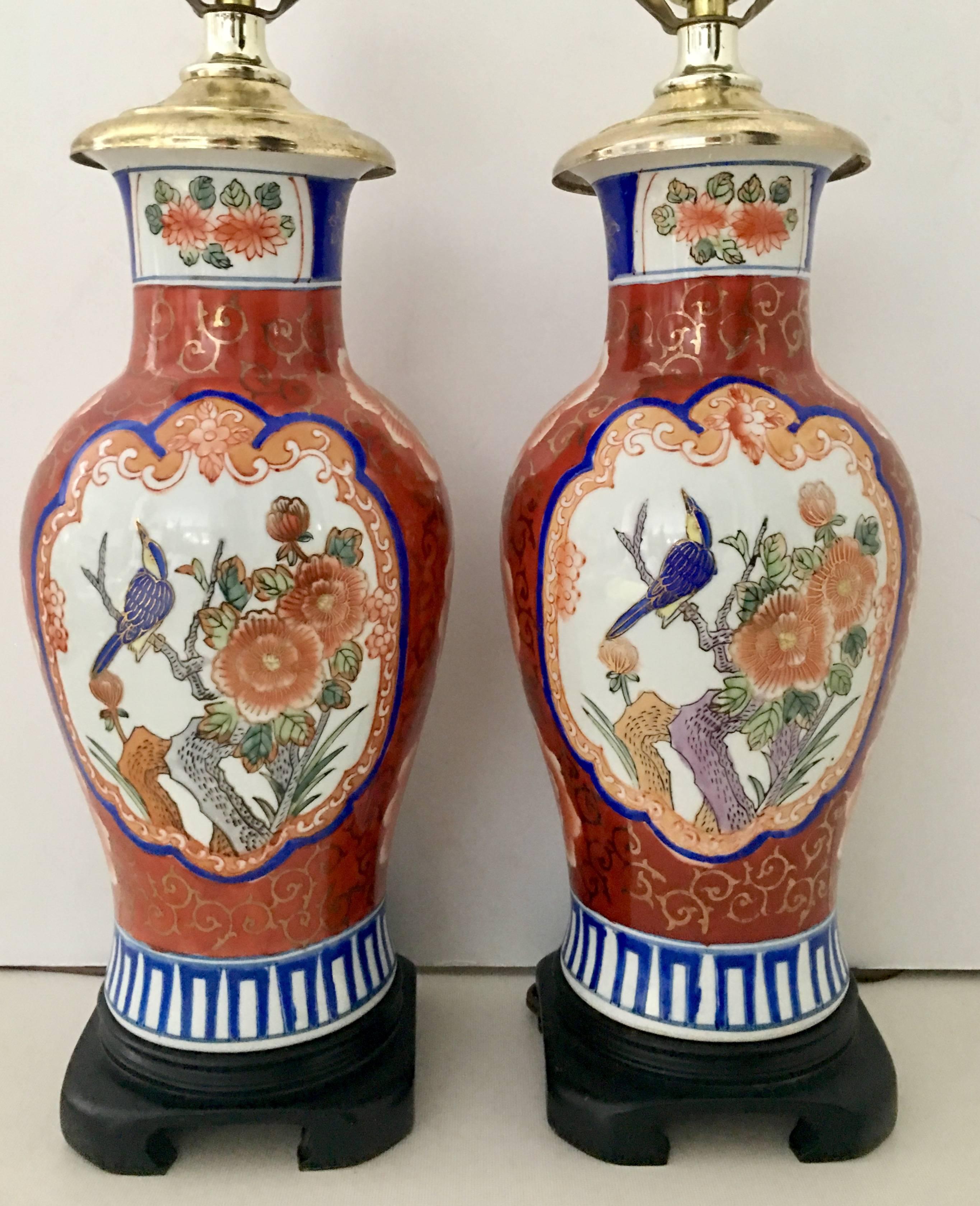 Gorgeous pair of Mid-Century porcelain hand-painted Imari table lamps. Features a central double-sided bird motif with bright shots of cobalt blue and 22-Karat gold accent. Bases are wood stained mahogany and neck caps made of brass. Includes brass