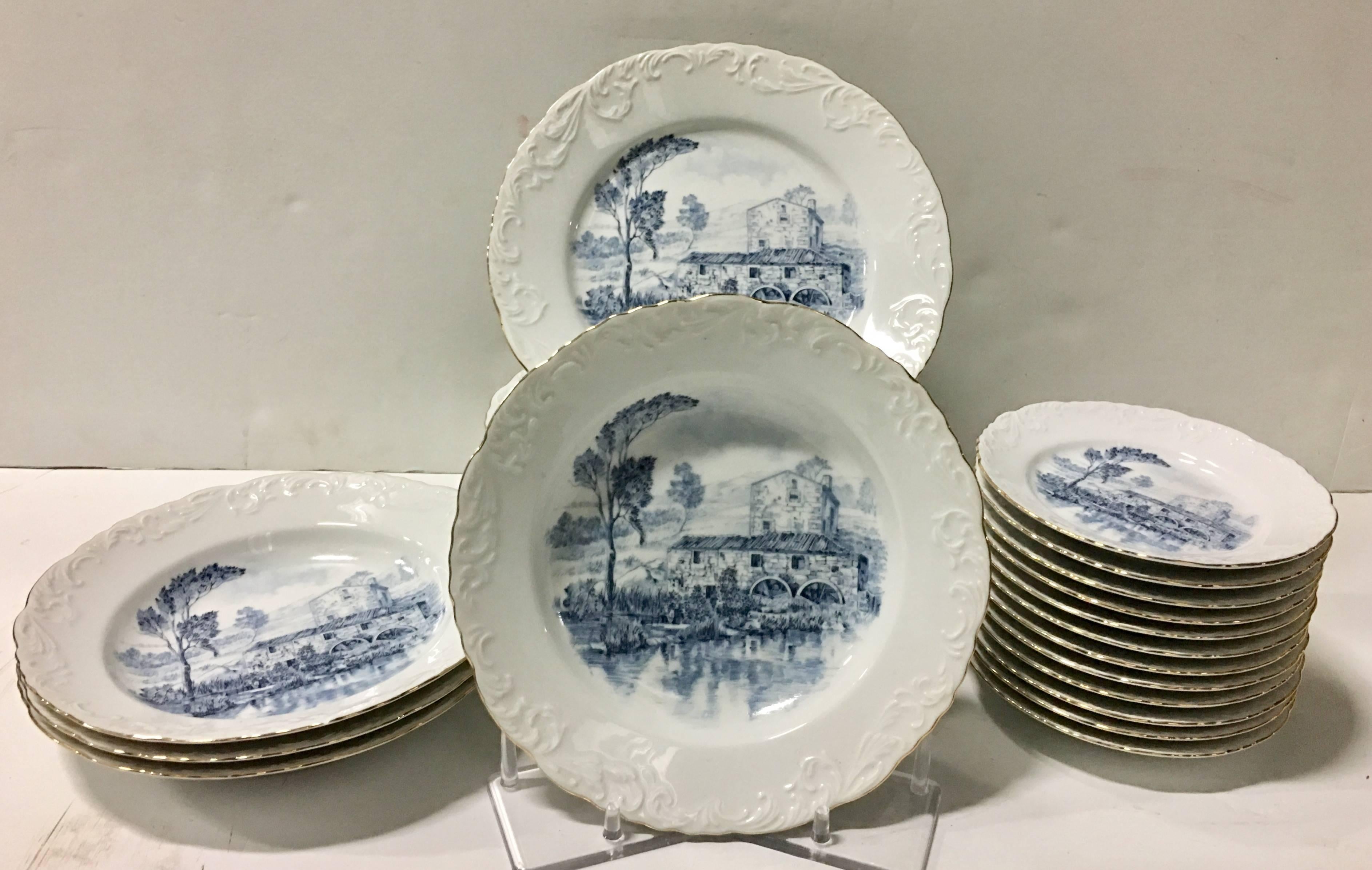 Vintage Portugal ceramic blue and white set of twenty six pieces by Spal Porcelanas. Pattern features a bright white ground with a blue country scene, raised embossed scroll detail edge and 22-karat gold rim. Set includes, ten dinner plates, nine