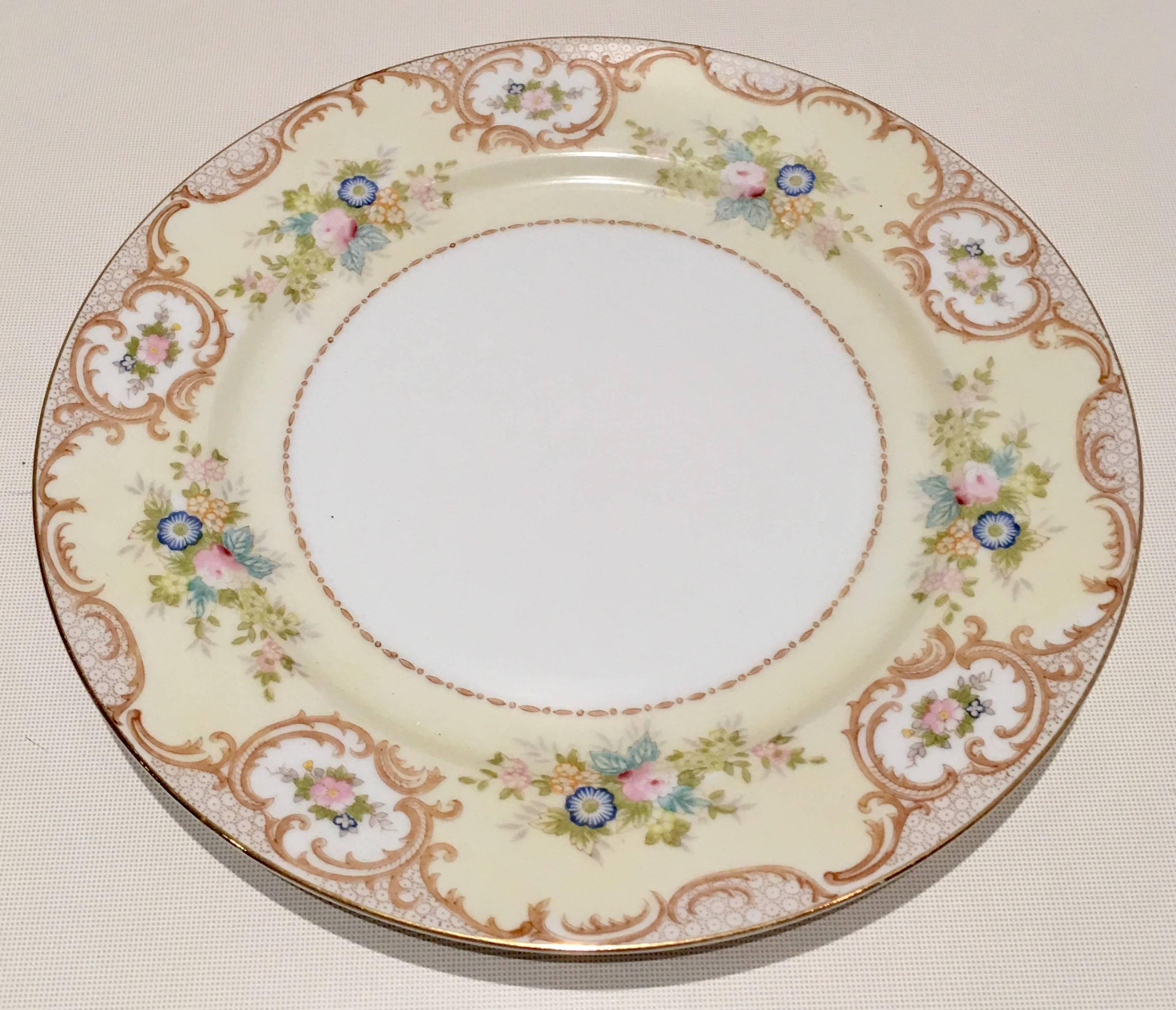 Vintage hand-painted Japanese porcelain set of nine dinner plates by, Meito China. Features a bright white ground with a creamy yellow border, decorated with gold scrolls with blue, pink and yellow floral bouquet and a 22-karat gold rim. Each piece