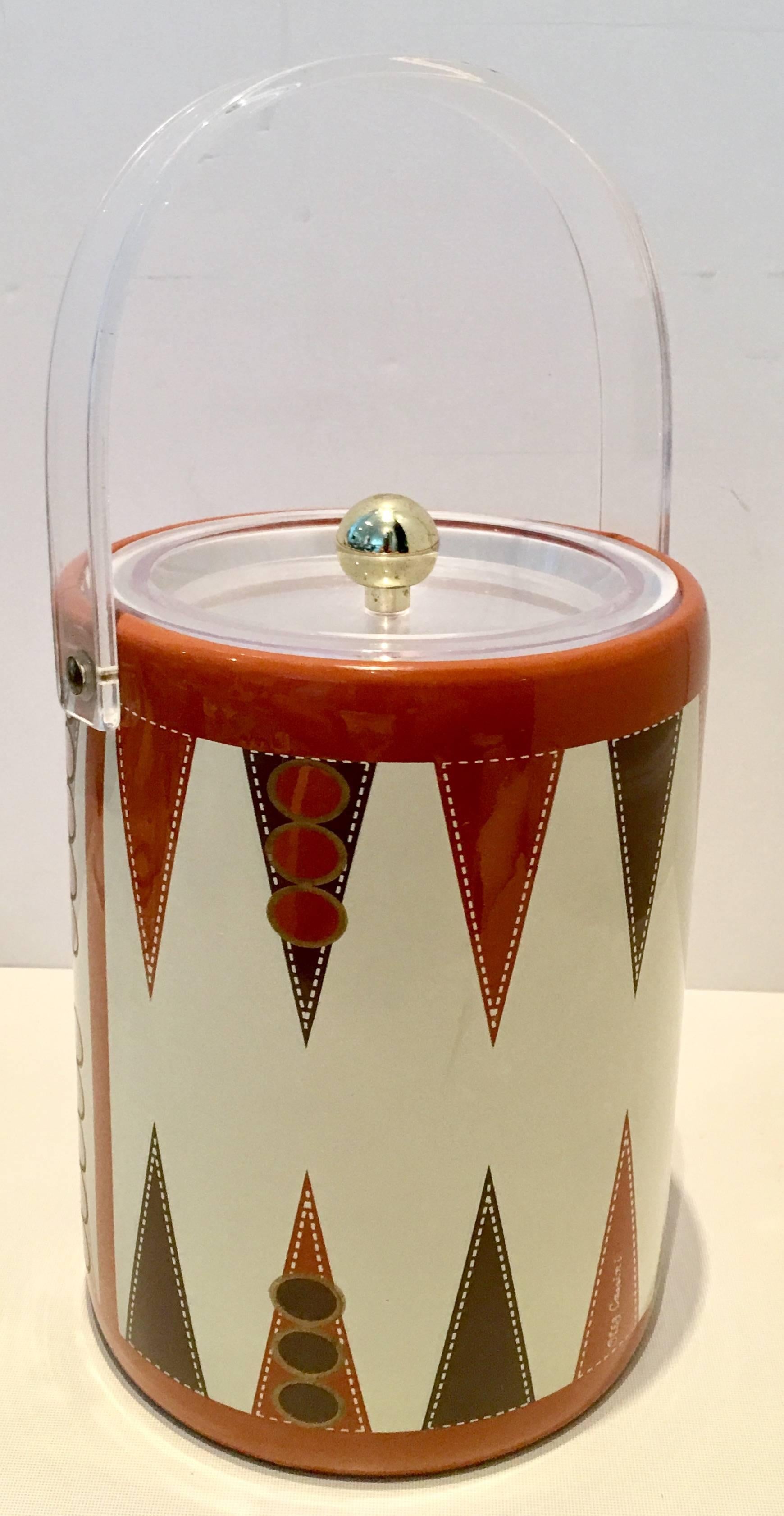 1970s Backgammon motif vinyl and Lucite thermal ice bucket by, Oleg Cassini.
Features a cream ground with burnt orange, brown, white and gold backgammon board motif. The handle is made of thick Lucite as well as the lid and features brass hardware.