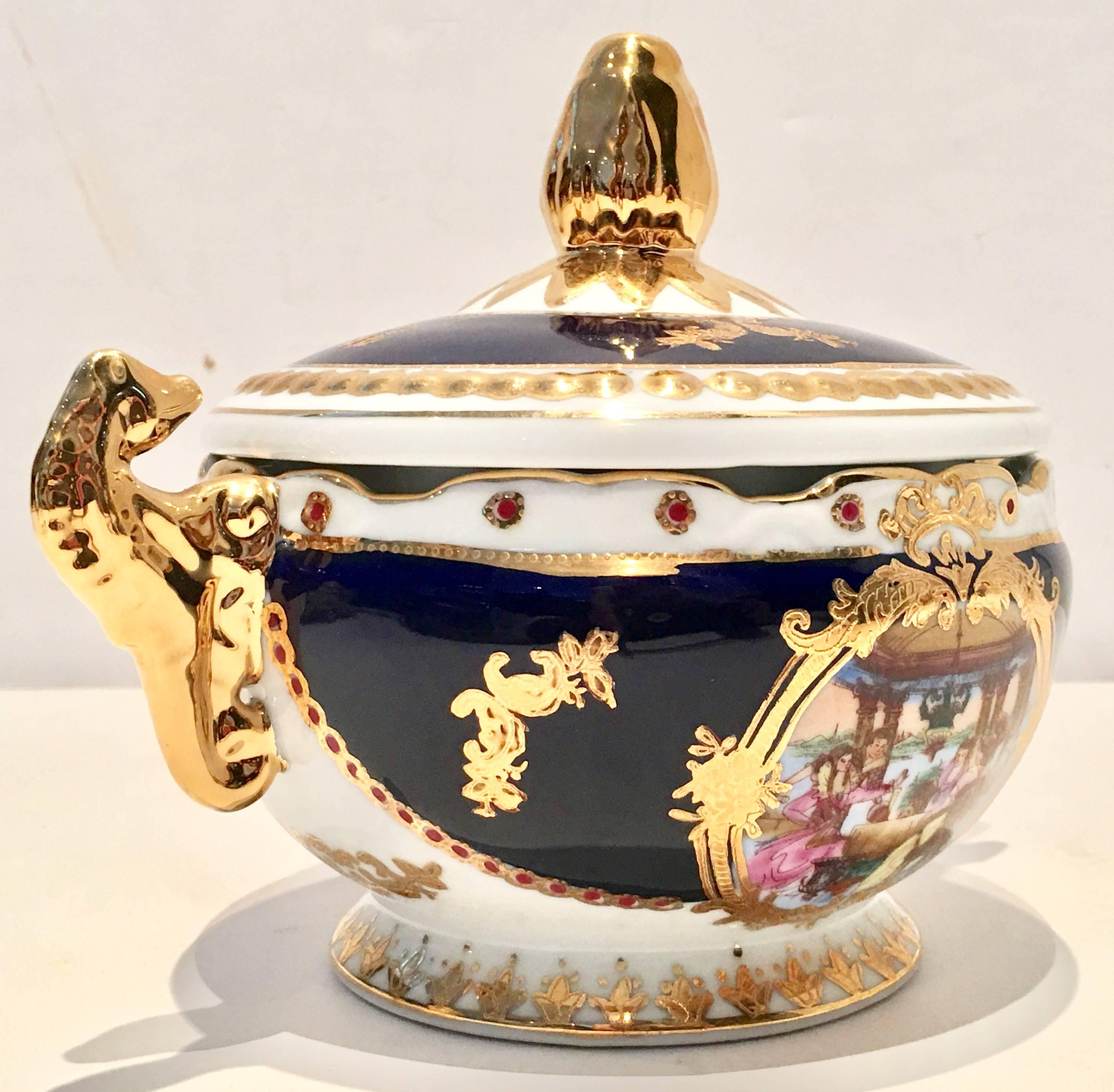 Mid-Century porcelain, Limoges cobalt and 22-karat gold lidded jar. This ornate and heavily gilded and decorated French Sèvres style two-piece lidded jar features a bright white and cobalt ground with a two sided 18th century group of diners eating