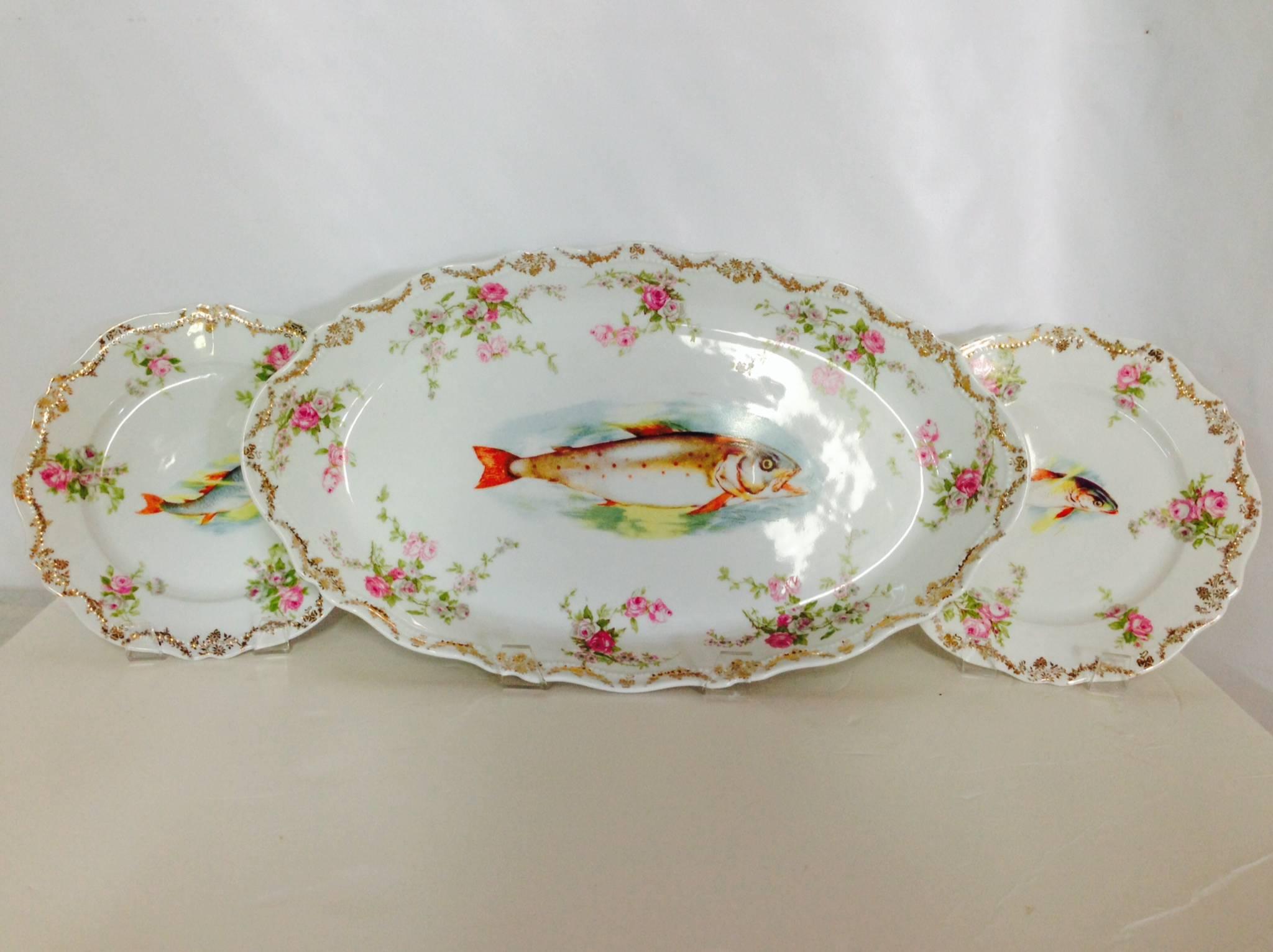 Very rare Oscar & Edgar Gutherz floral fish serving set of 13 Pieces. This set includes twelve fish plates and one large oval serving platter. Hand-painted pink and green rose pattern border on a white ground. Orange, blue and yellow central