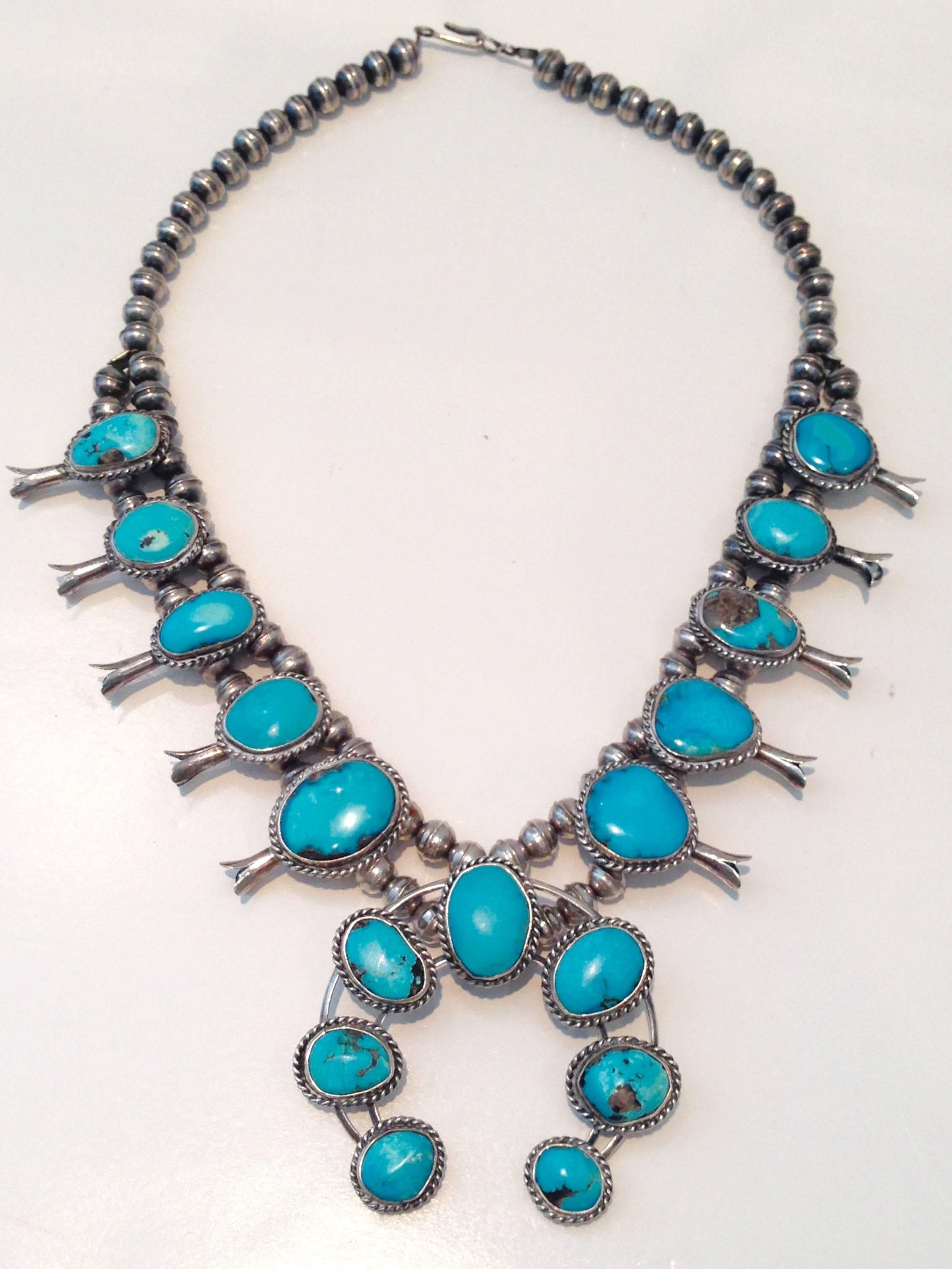 1960s Navajo-style old pawn sterling silver and brilliant turquoise squash blossom necklace. This piece of art has a total of 17 turquoise polished stones and double silver bead detail. Each of the 10 side stones measure. 75