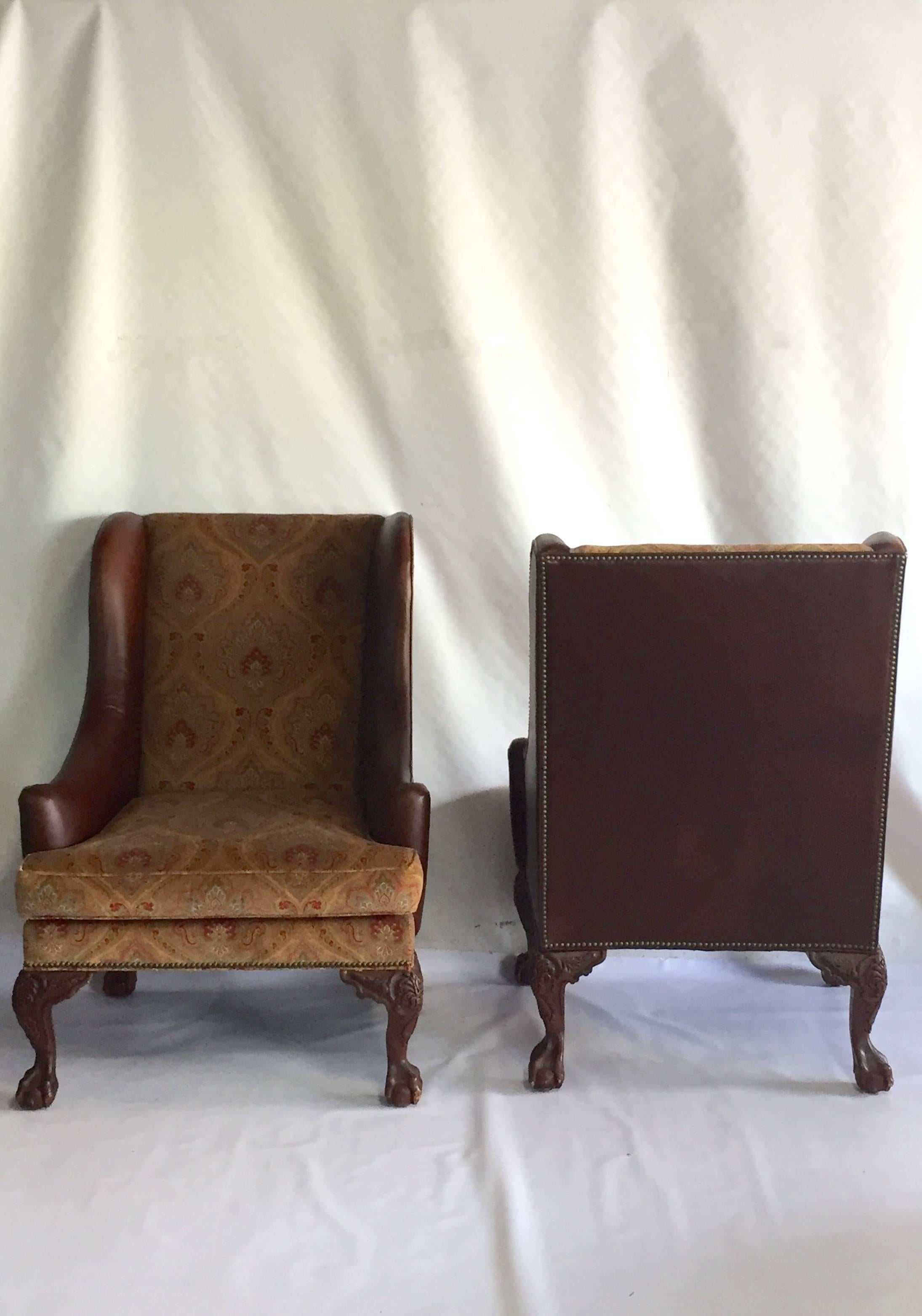 1980s leather and fabric upholstered George II style high back wing chairs and ottoman three-piece set. Four hand-carved cabriole claw foot legs, brass nailhead detail with chocolate leather and a velvet blend paisley patterned fabric. Seat cushions