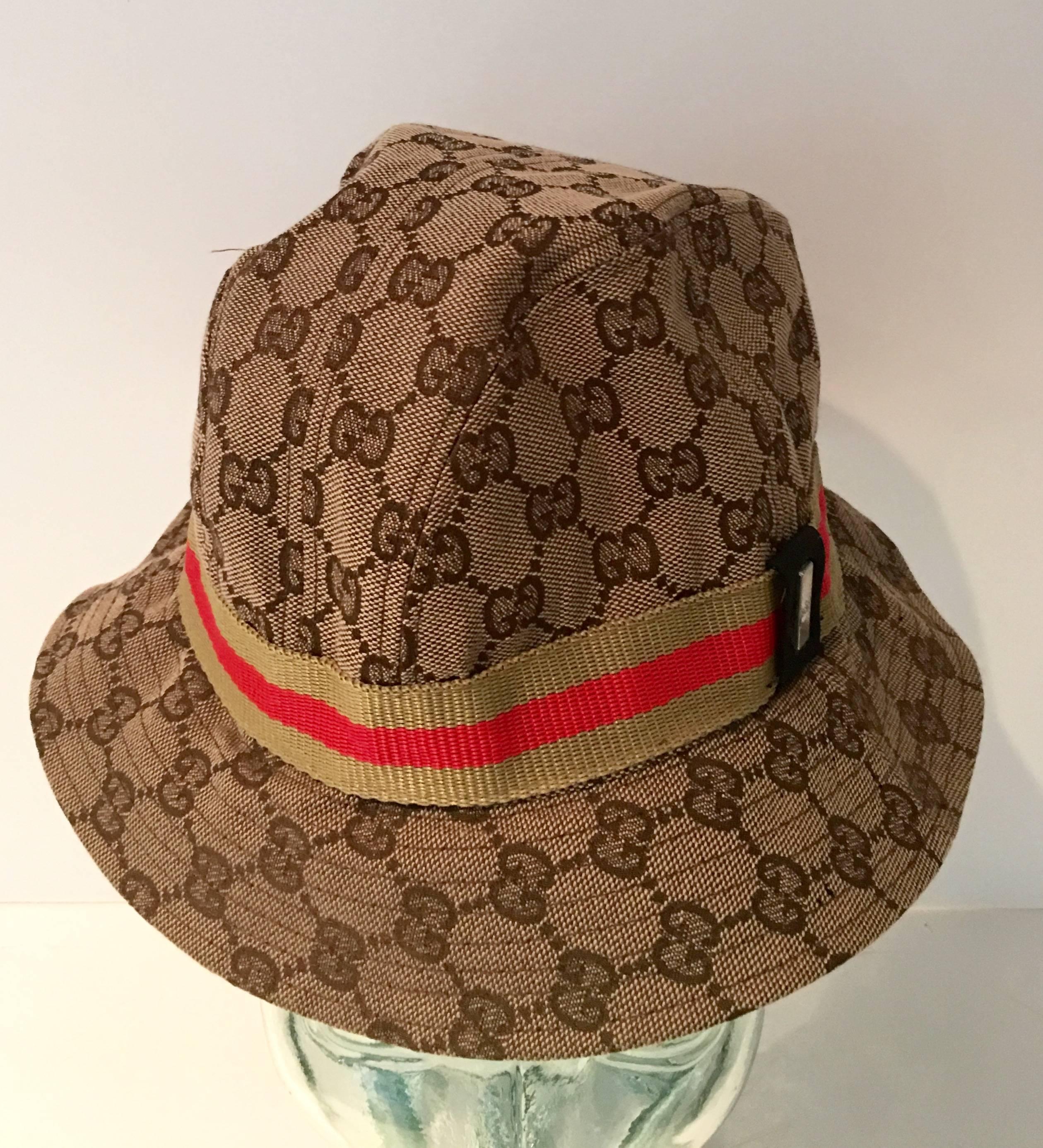 This iconic floppy fedora hat made in Italy by, Gucci is tan canvas with a khaki and bright red stripe band and silver tone Gucci log tag detail set on black fabric. Gucci label intact, children's size large or female adult size small. Interior size
