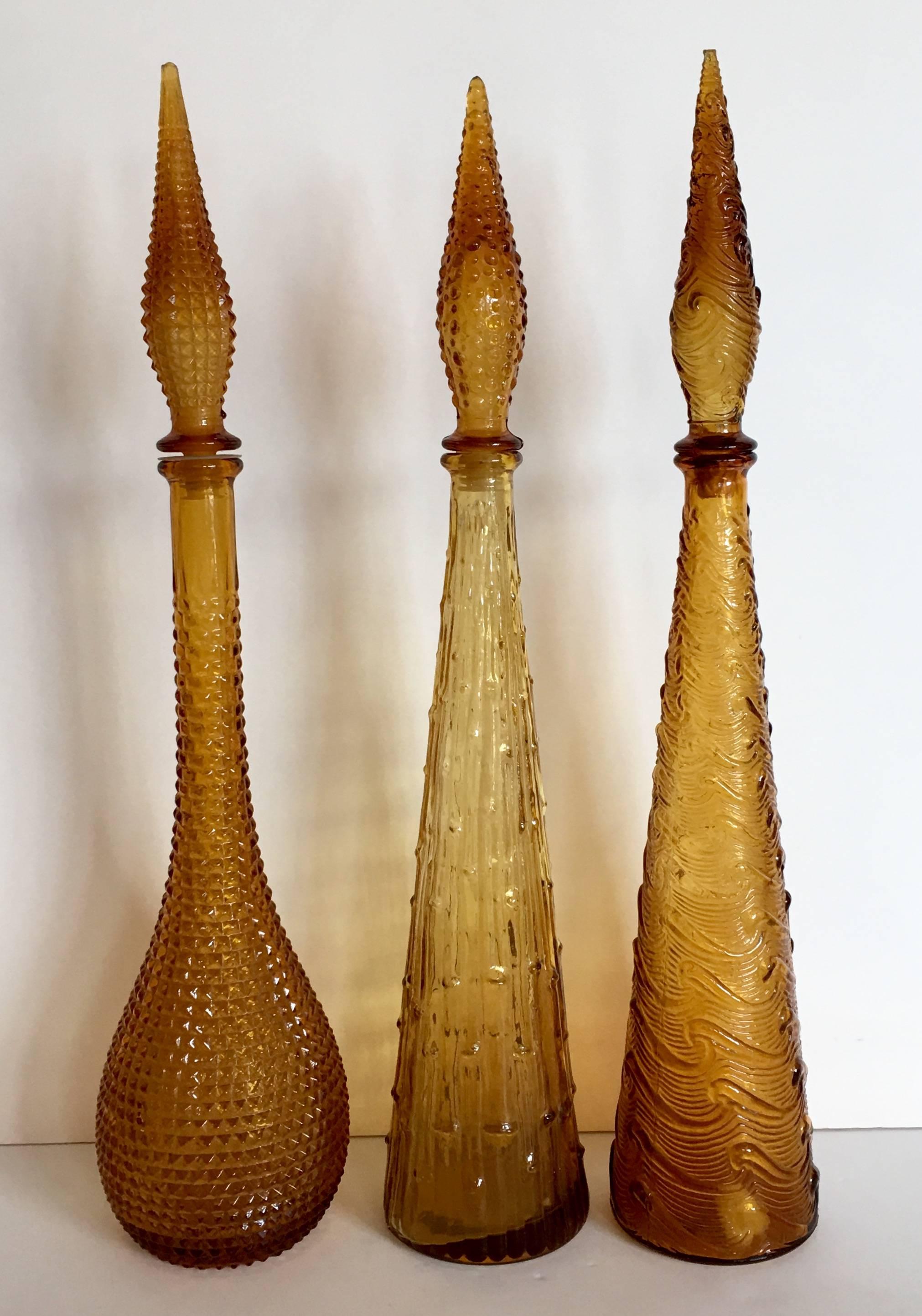 Set of three amber textured Italian Empoli glass decanters. Each one has a different pattern and all are signed Italy on the underside. Set includes one faceted pattern, one faux bamboo pattern 22.25" height x 4.25" diameter and one wave