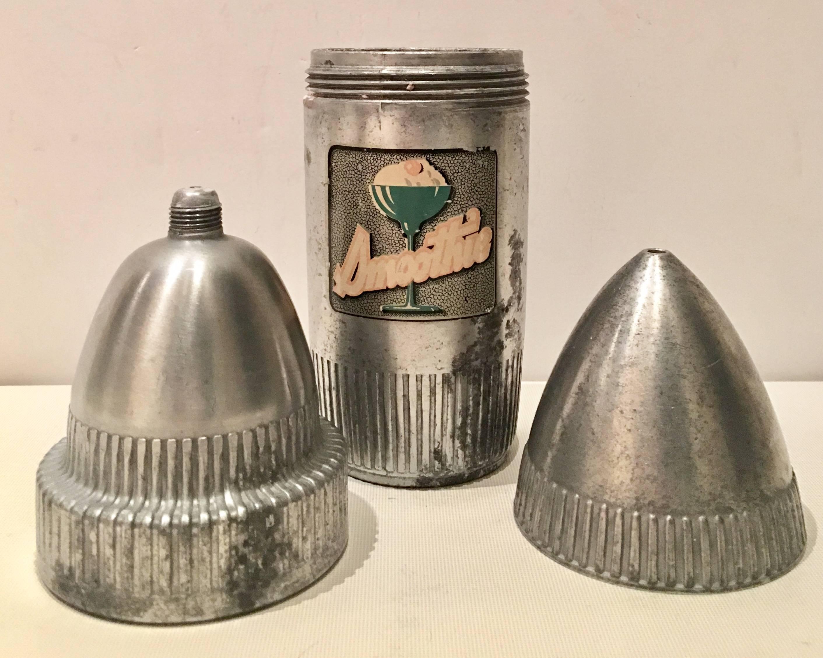 Vintage steel atomic bullet smoothie or cocktail shaker. Features three pieces, the bottom, the interior top with a hole at the top centre for beverage pouring and the top. Both tops screw in place. The bottom has a central soda fountain motif in