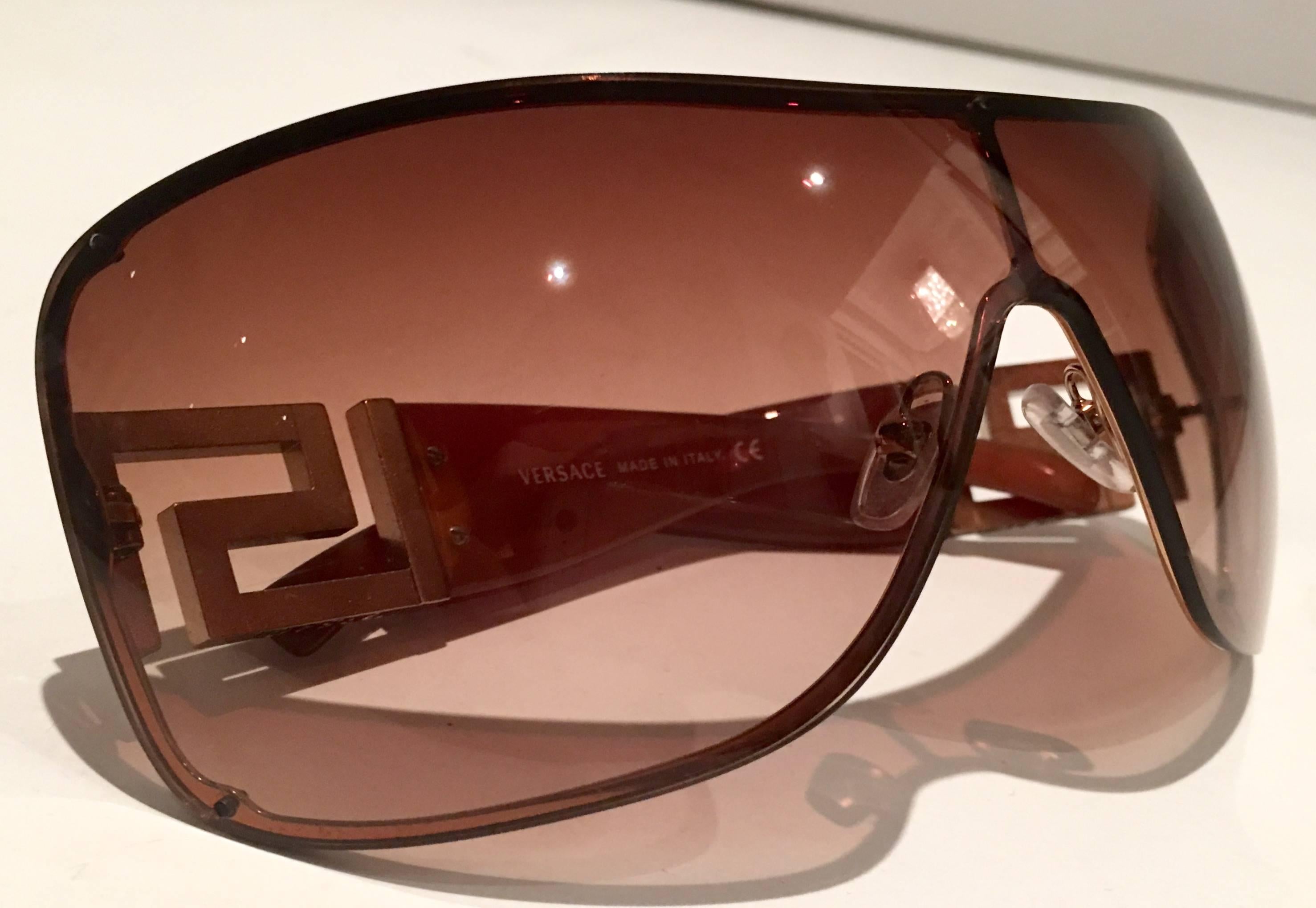 Rare Versace brown and gold aviator shield style sunglasses. Features baguette cut Swarofski rhinestone Greek key arm detail. Includes soft white authentic Versace protective storage case. Model 2072-B, Made In Italy.