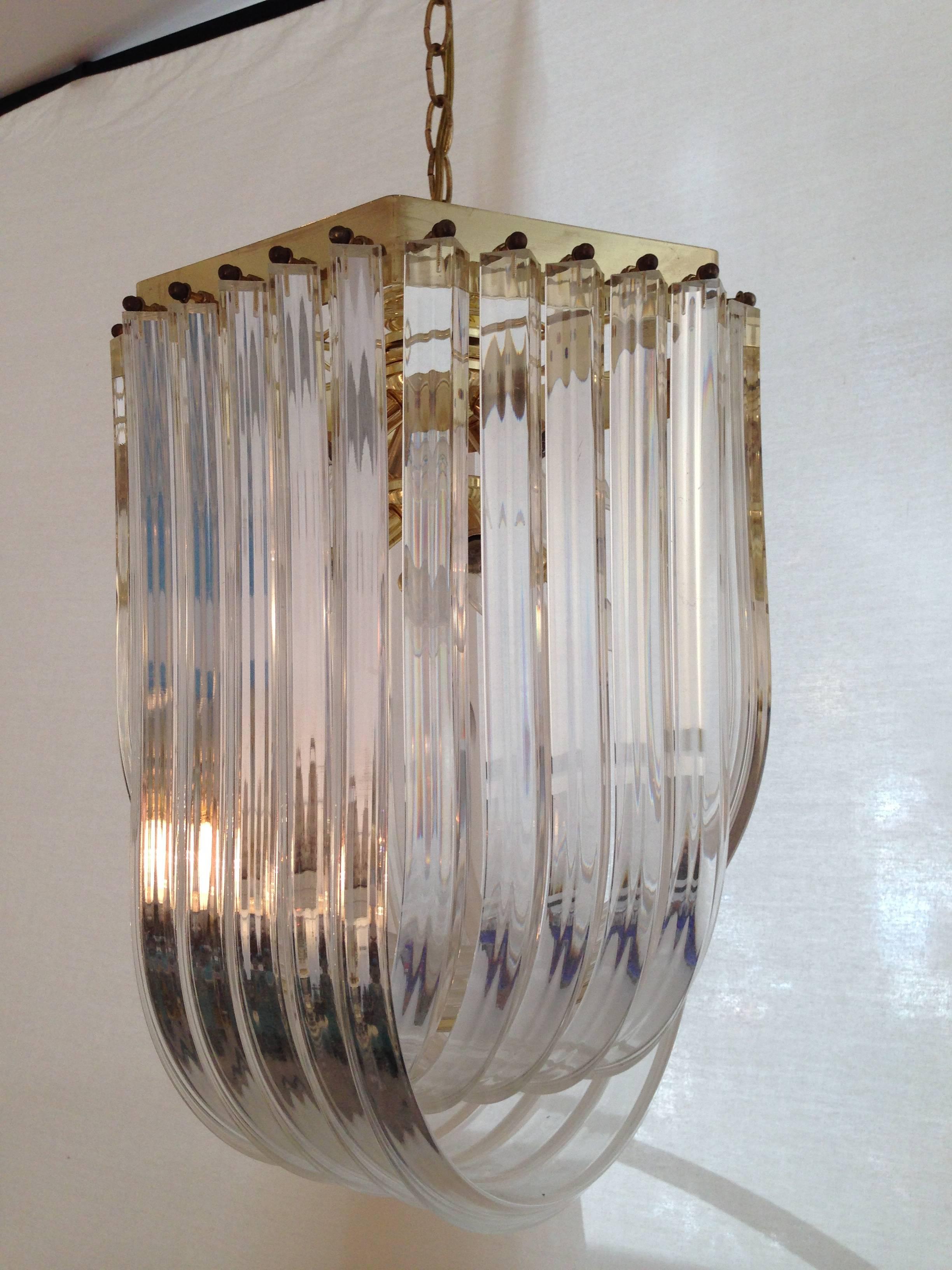 1970s Modern Lucite tube and brass ribbon swag chandelier. Includes 19" L brass link chain. Wired for the US and in working order. Takes ten 40W-max candelabra style bulbs.