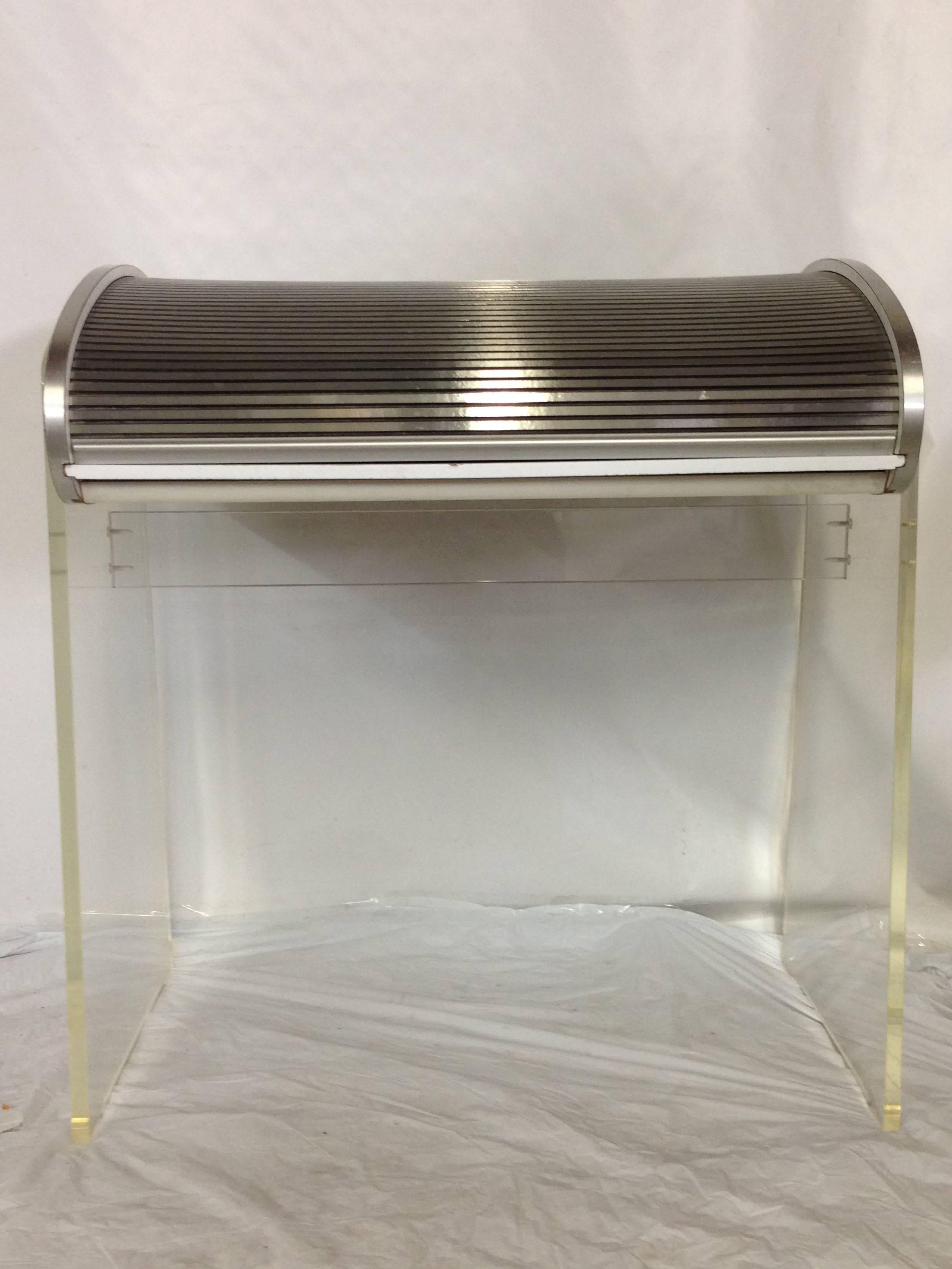 In the style of Vladimir Kagan, this rare and unique twist on the Classic roll-top desk is a stunner. Thick Lucite side panel legs are attached with large round chrome screw head detail. Brushed aluminum slat roll top mechanism. Laminated wood