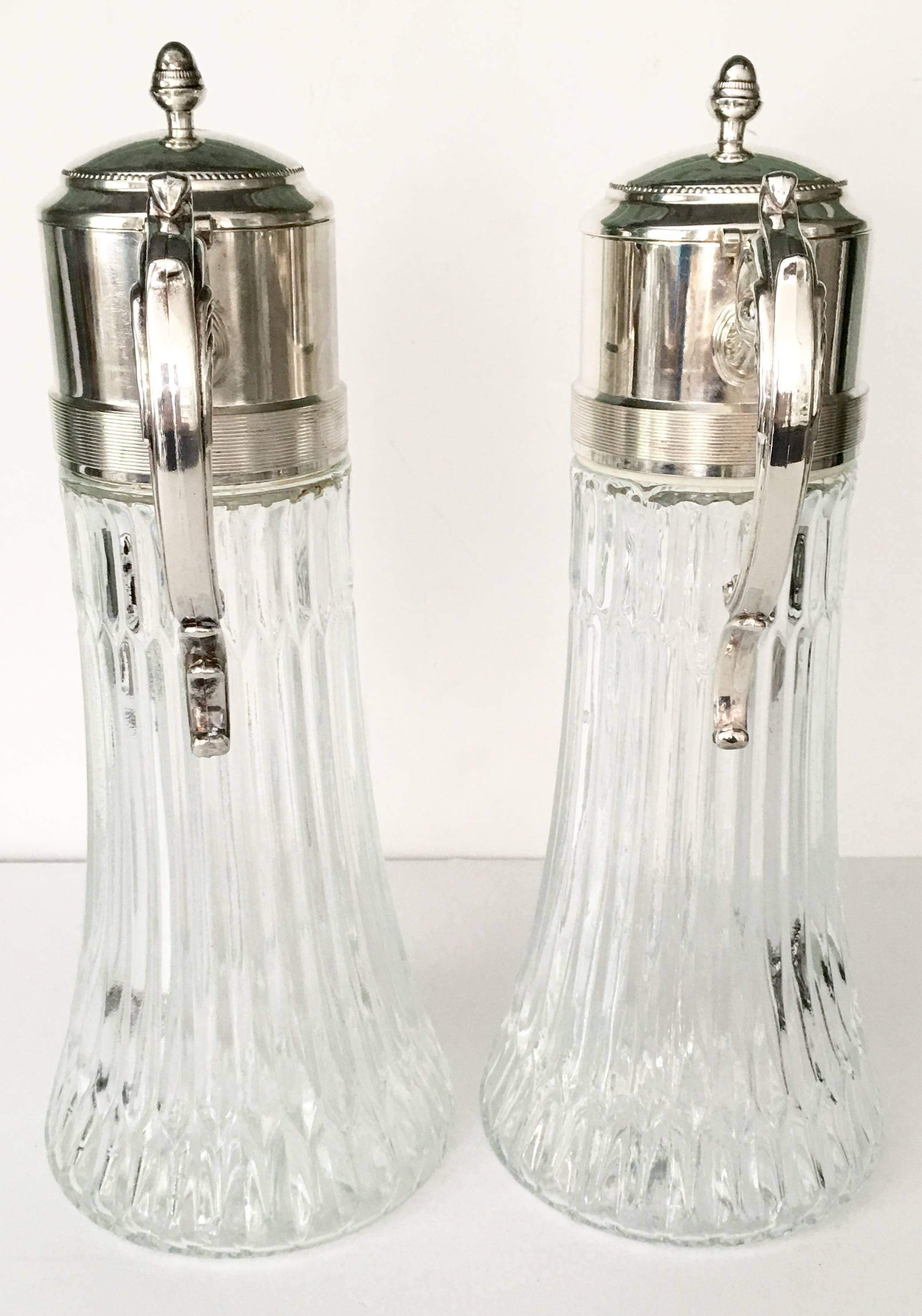 Mid-20th century brilliant cut-glass and silver plate scroll motif handle screw top claret pitcher jugs. Each handle is slightly different at the bottom. One top is signed or hallmarked.