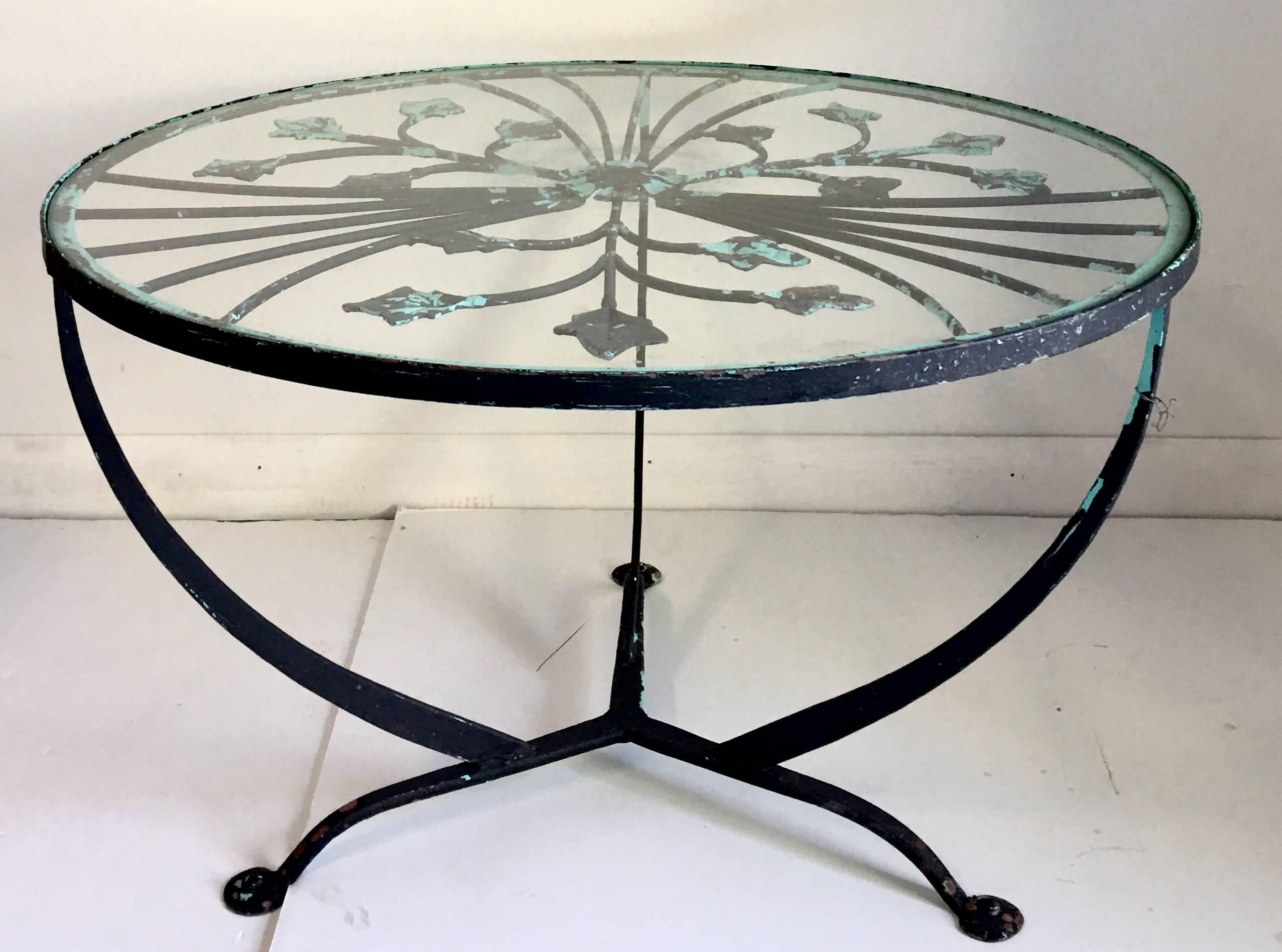 Vintage hand-forged wrought iron French Art Deco style foliate glass top cocktail table. Features a three leg tripod base and painted in distressed verdigris green. Includes a glass top.