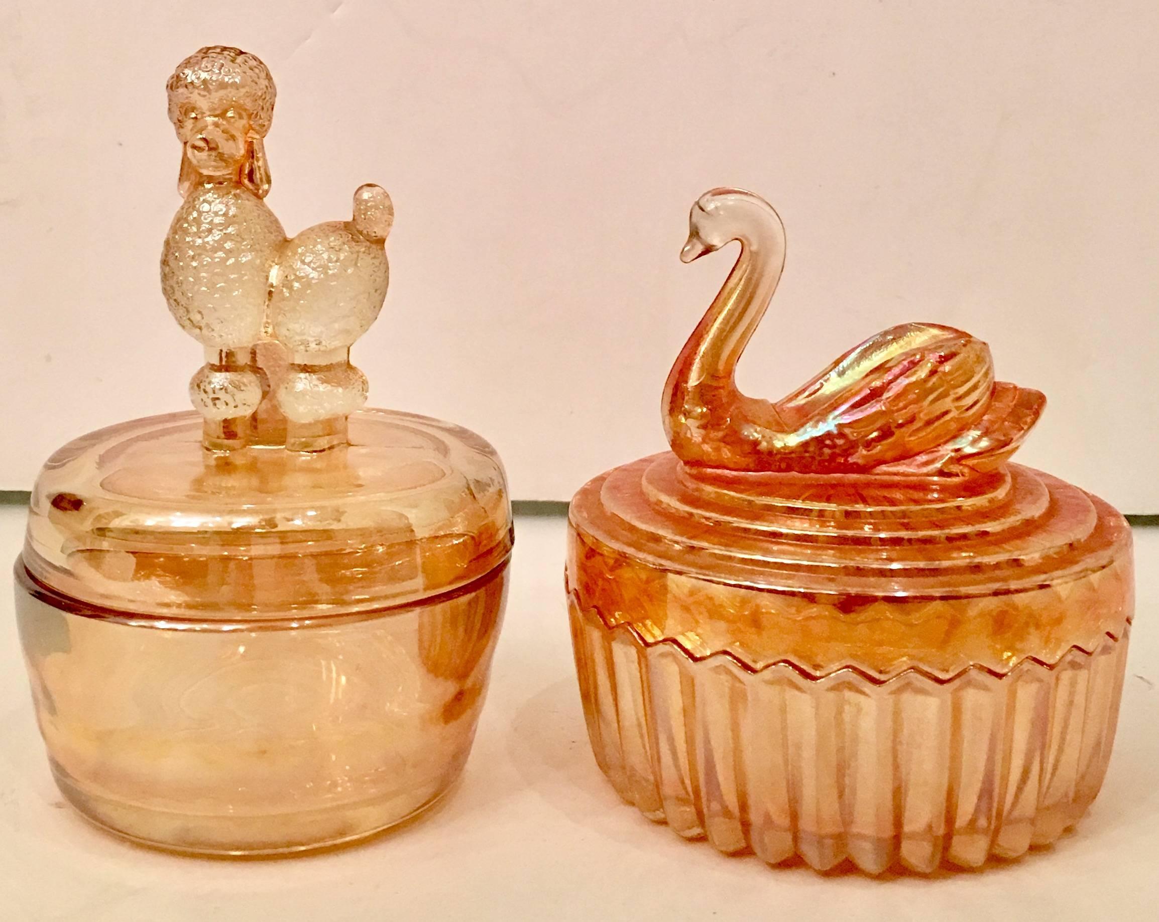 Mid-Century pair of peach luster glass lidded vanity jars. The pair consists of one lidded jar with a figural poodle centered on the lid and one with a figural swan that has a cut-out slope on his back for placing a trinket. 
The swan lidded jar