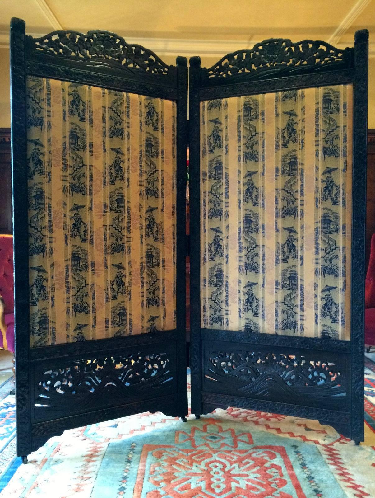 A large antique Victorian 19th century ebony Chinese heavily carved two-panel screen, twin painted panels to one side featuring painted birds on terra cotta red lacquered panels with ornate carvings to the top and base, the reverse side upholstered