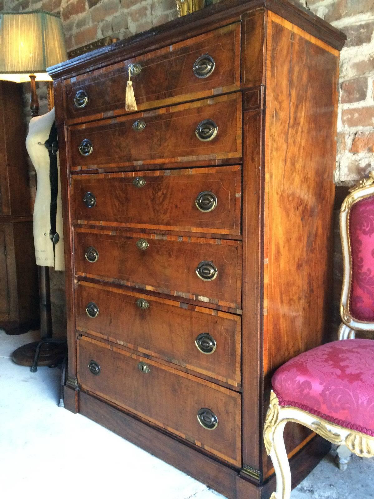 An old scarred and battered antique Georgian flame fronted mahogany and fruitwood cross banded tallboy chest of drawers, rectangular top over six boxwood inlaid graduated drawers including a secretaire drawer with fitted interior, original oval