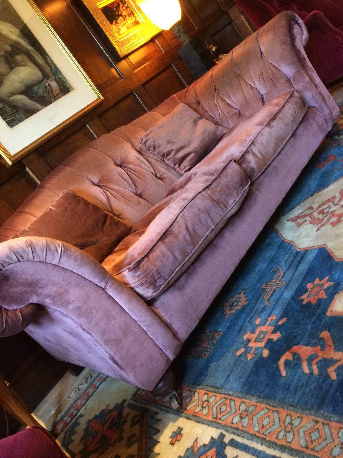 A Liberty & Co Chesterfield three-seat button back sofa, having arched back, scrolling shaped arms and turned front legs with casters, upholstered in ’Lilac’ velvet, the sofa is offered in good vintage condition with solid joints and no sagging or