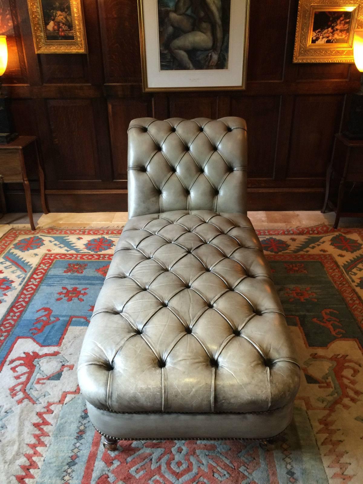 A leather club style Chesterfield button-back chaise longue couch with scrolling ends and standing on four turned legs terminating in brass casters, upholstered in grey or very light green leather.