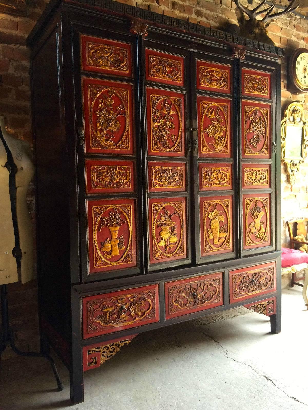 Antique early 20th century Chinese lacquered chinoiserie four-door wardrobe armoire decorated in red and gold lacquer, the doors and base heavily decorated with embossed flowers, corniced top with ‘Greek Key’ design over four cupboard doors with