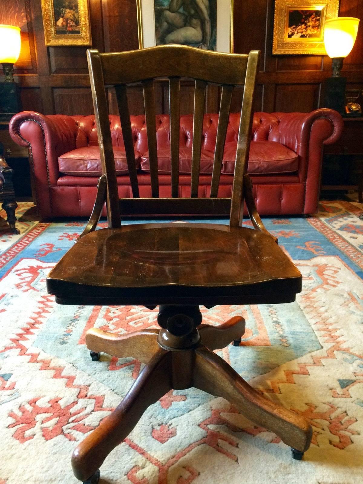 Antique vintage oak rotating and reclining office chair standing on four splayed legs with casters.