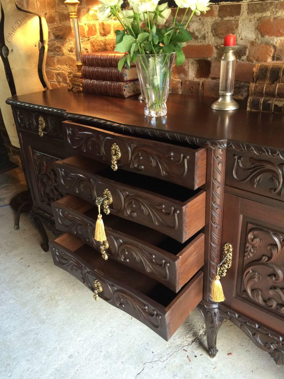 A profusely carved Spanish style solid oak sideboard credenza, the solid serpentine top over a central bank of four heavily carved drawers with a pair of frieze drawers and a pair of cupboards either side all with scrolled brass escutcheons over